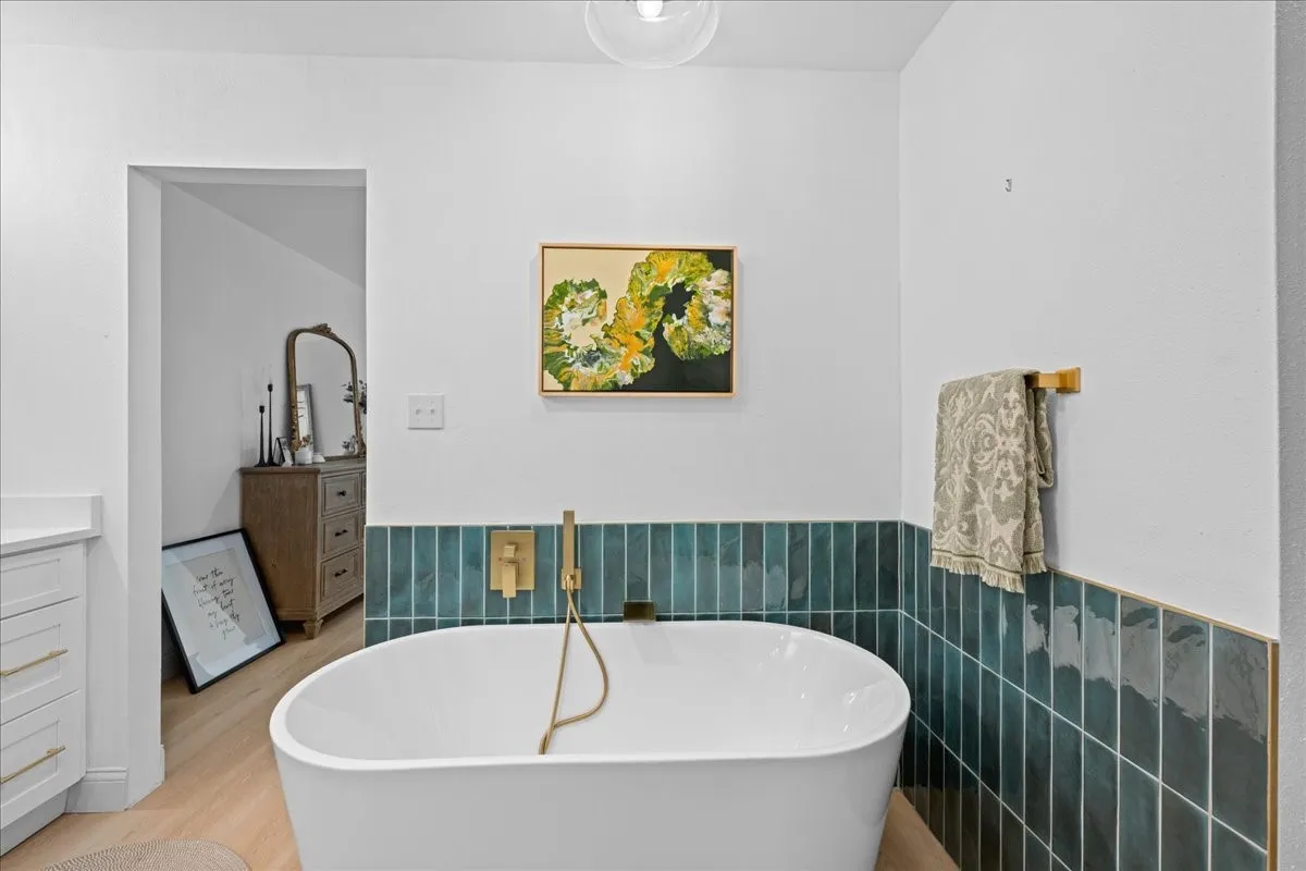 Freestanding soaking tub with a wall-mounted brass faucet, complemented by teal subway tile wainscoting