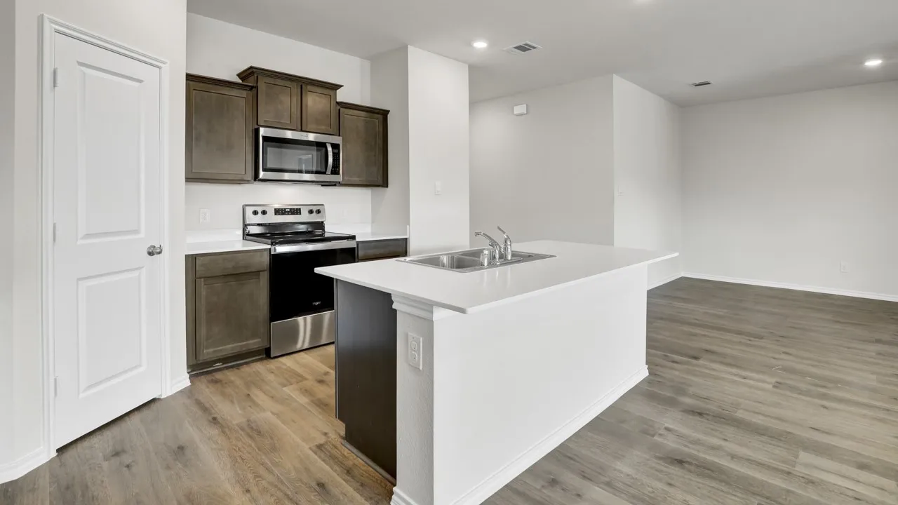 Kitchen featuring wood-finish flooring, stainless steel appliances, dark wood cabinetry, white countertops, and a double basin sink