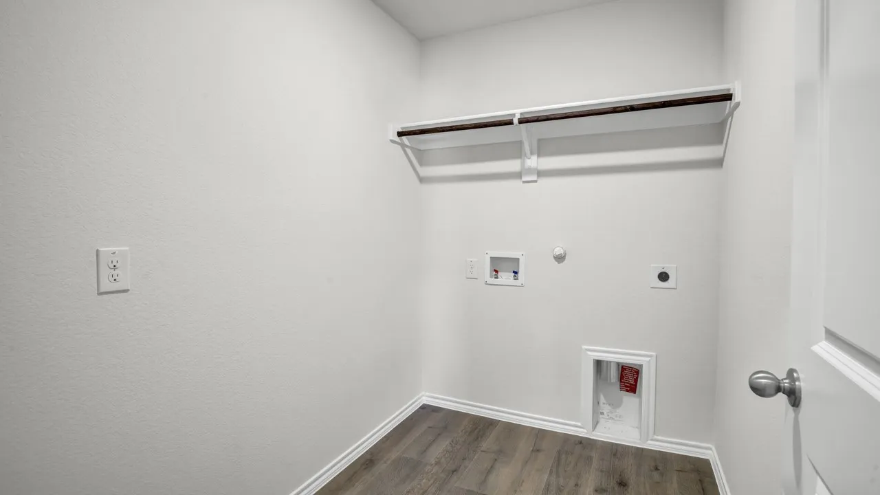 Wood-finish flooring with white baseboards, a built-in shelf with a clothing rod, and visible utility hookups