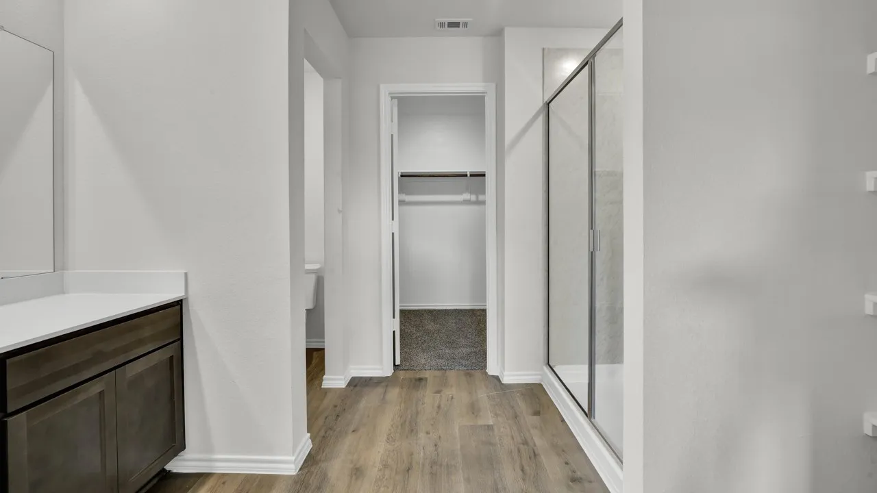 Wood-finish flooring, built-in vanity with white countertop, glass-enclosed shower, and a walk-in closet with shelving