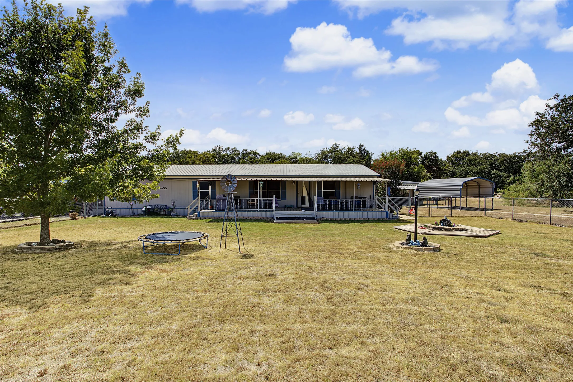Extensive outdoor space featuring a covered front porch, a detached carport, mature trees, and perimeter fencing