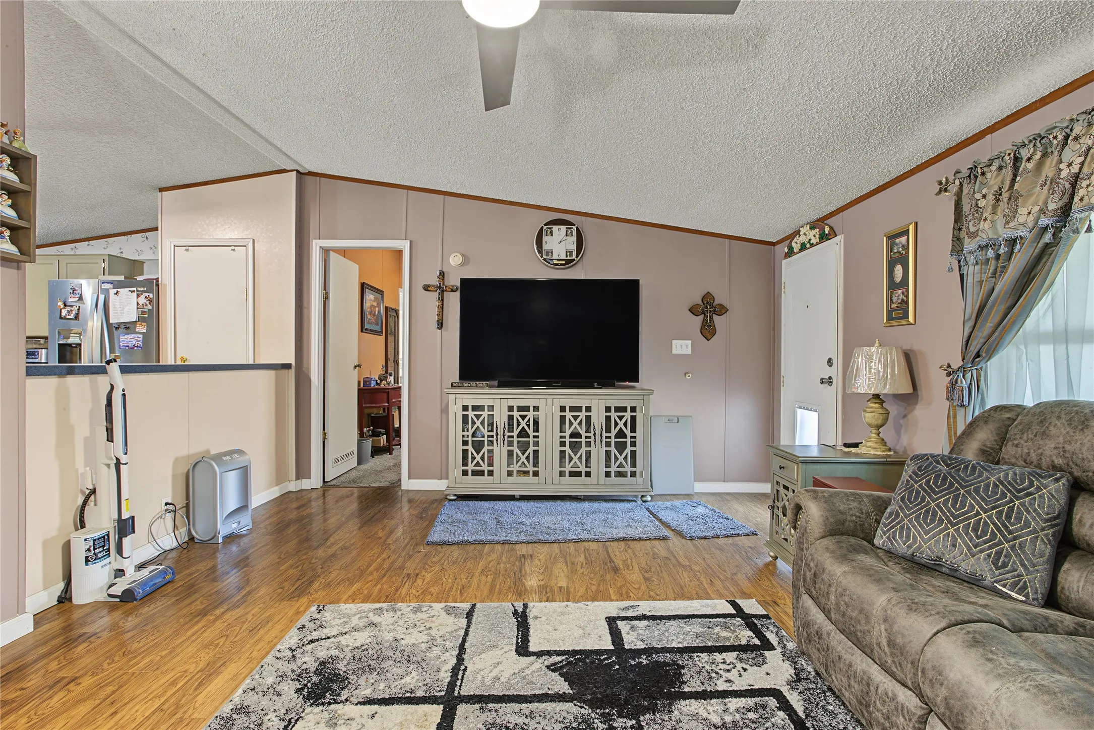 Wood-finish flooring throughout, ceiling fan with integrated lighting, and a kitchen pass-through window with a lower half-wall