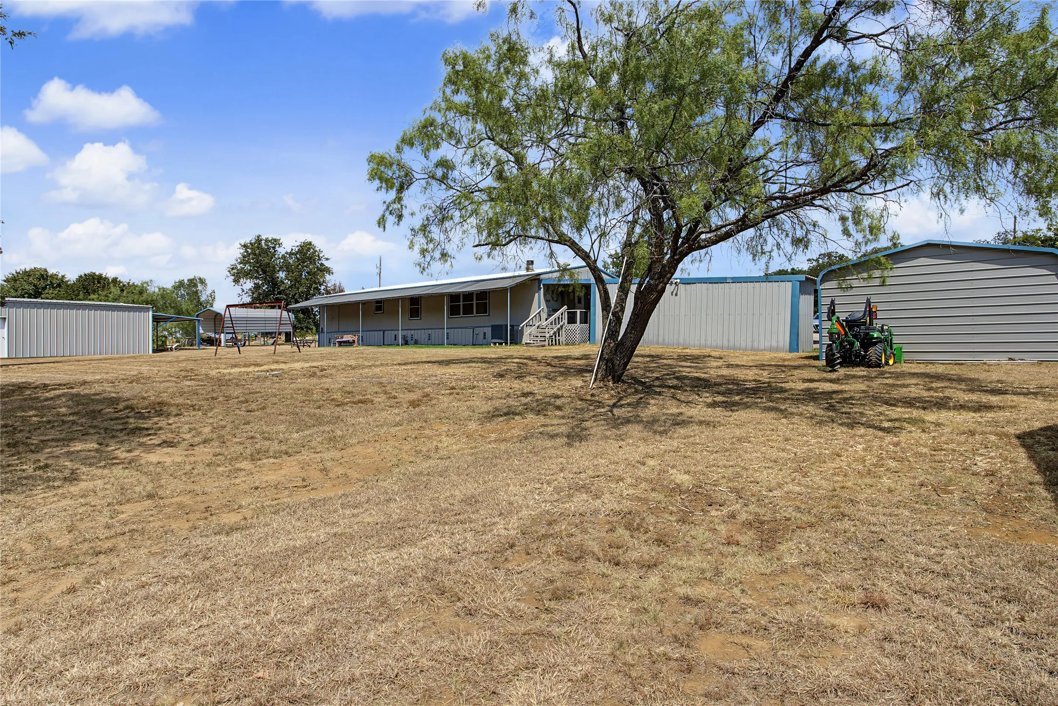 Expansive property with a single-story residence and multiple outbuildings, featuring a large tree providing shade