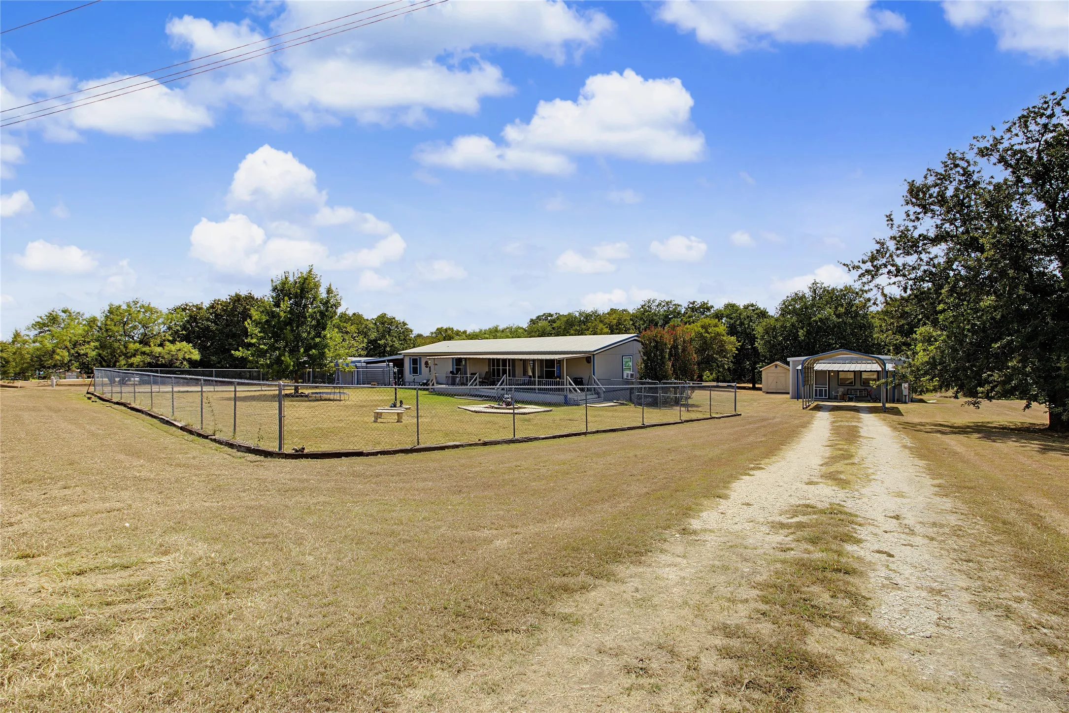 Expansive property featuring a gravel driveway, chain-link fenced yard, detached shed, and mature trees