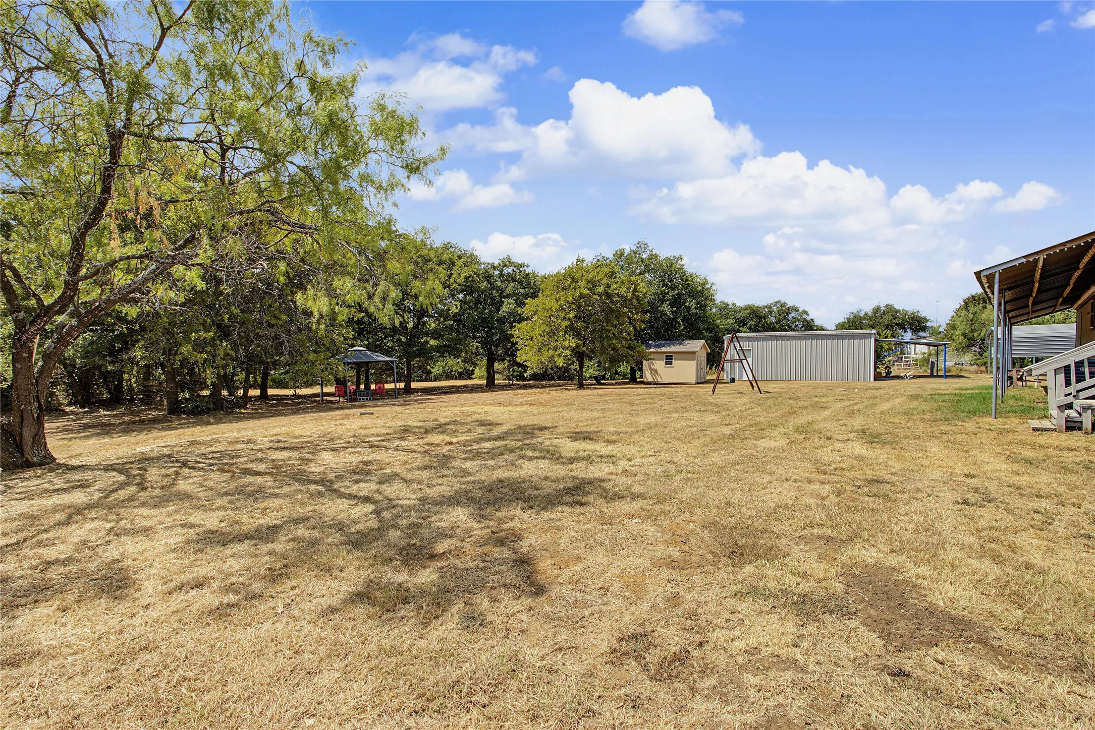 Expansive outdoor space featuring mature trees, a metal storage building, and a freestanding shed