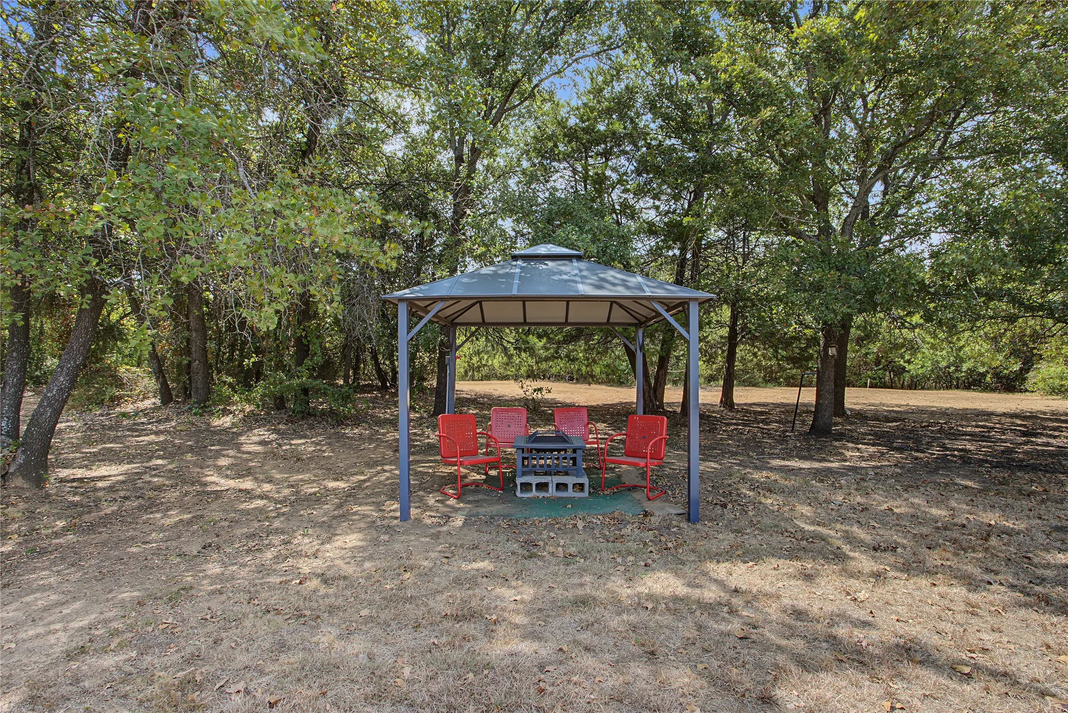 Outdoor gazebo structure with a metal frame and canopy, surrounded by mature trees