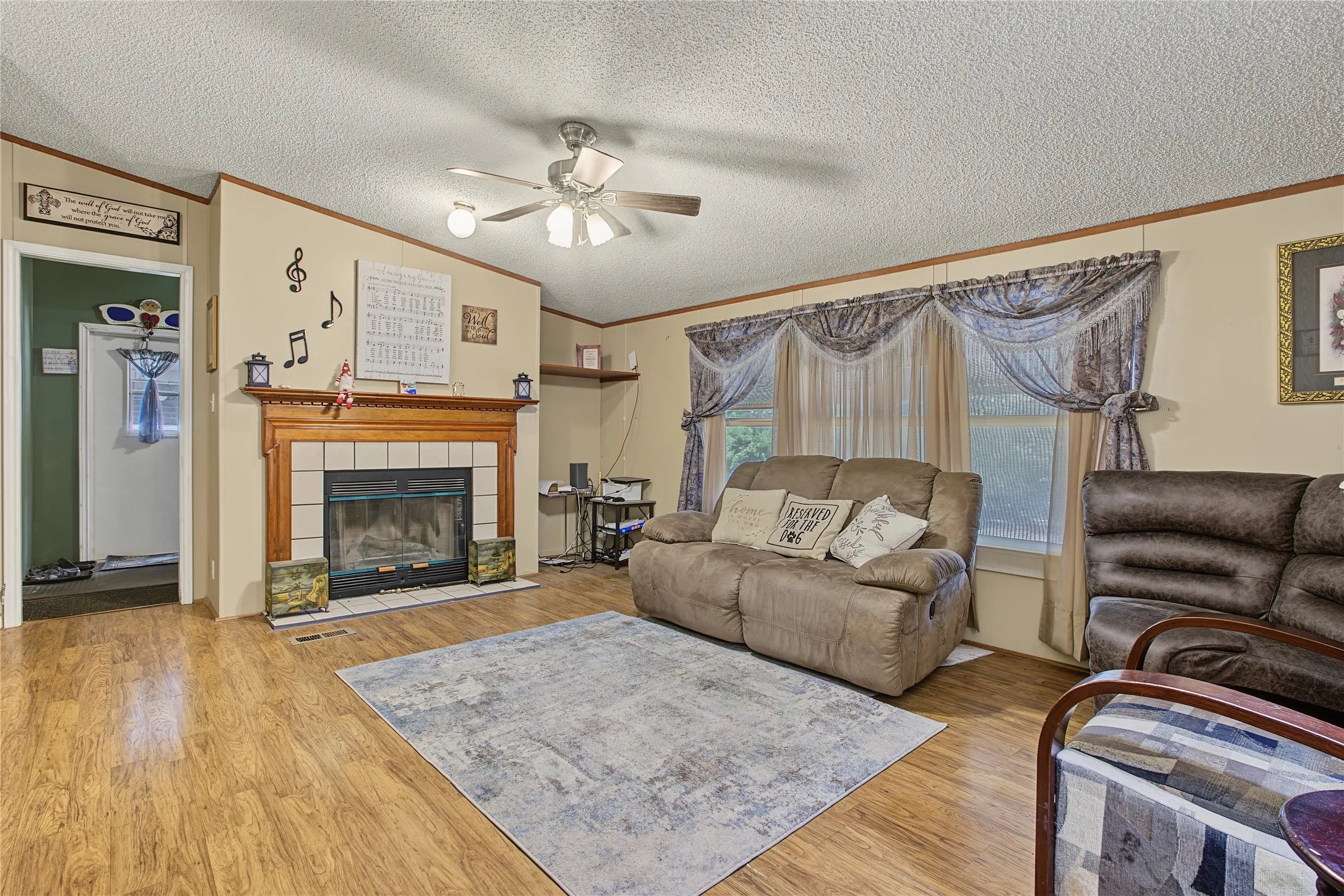 Wood-finish flooring, built-in fireplace with tile surround, wood mantel, ceiling fan with integrated lighting, and multiple windows