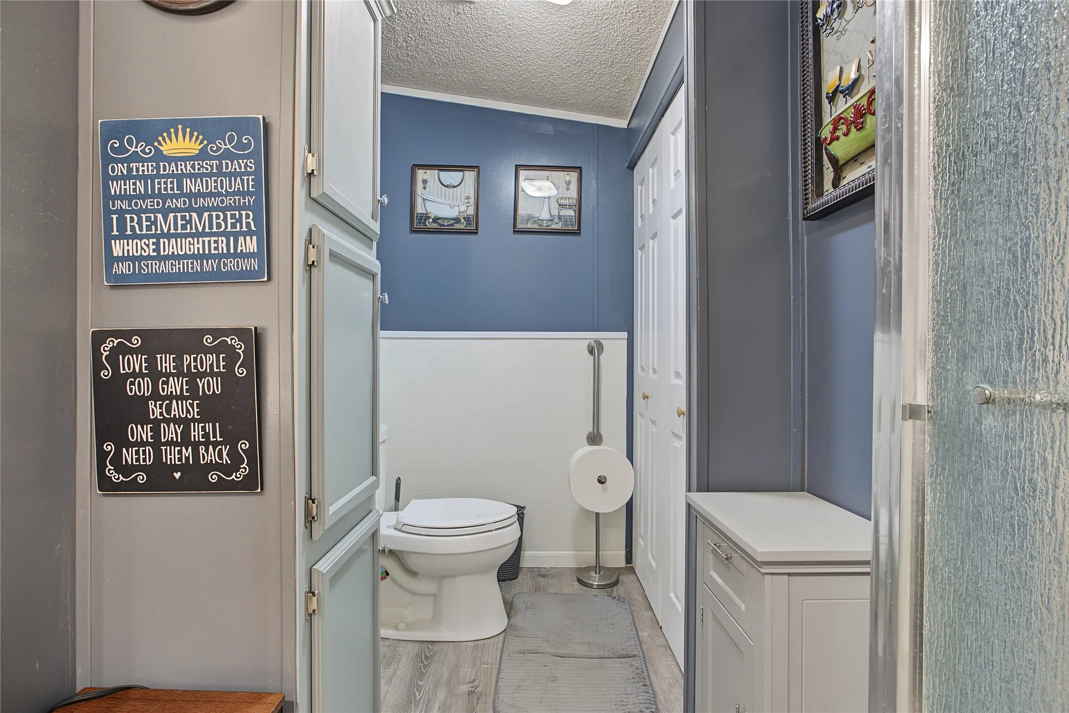 Bathroom featuring wood-finish flooring, two-tone wall paneling, built-in cabinetry, and a walk-in shower with textured glass
