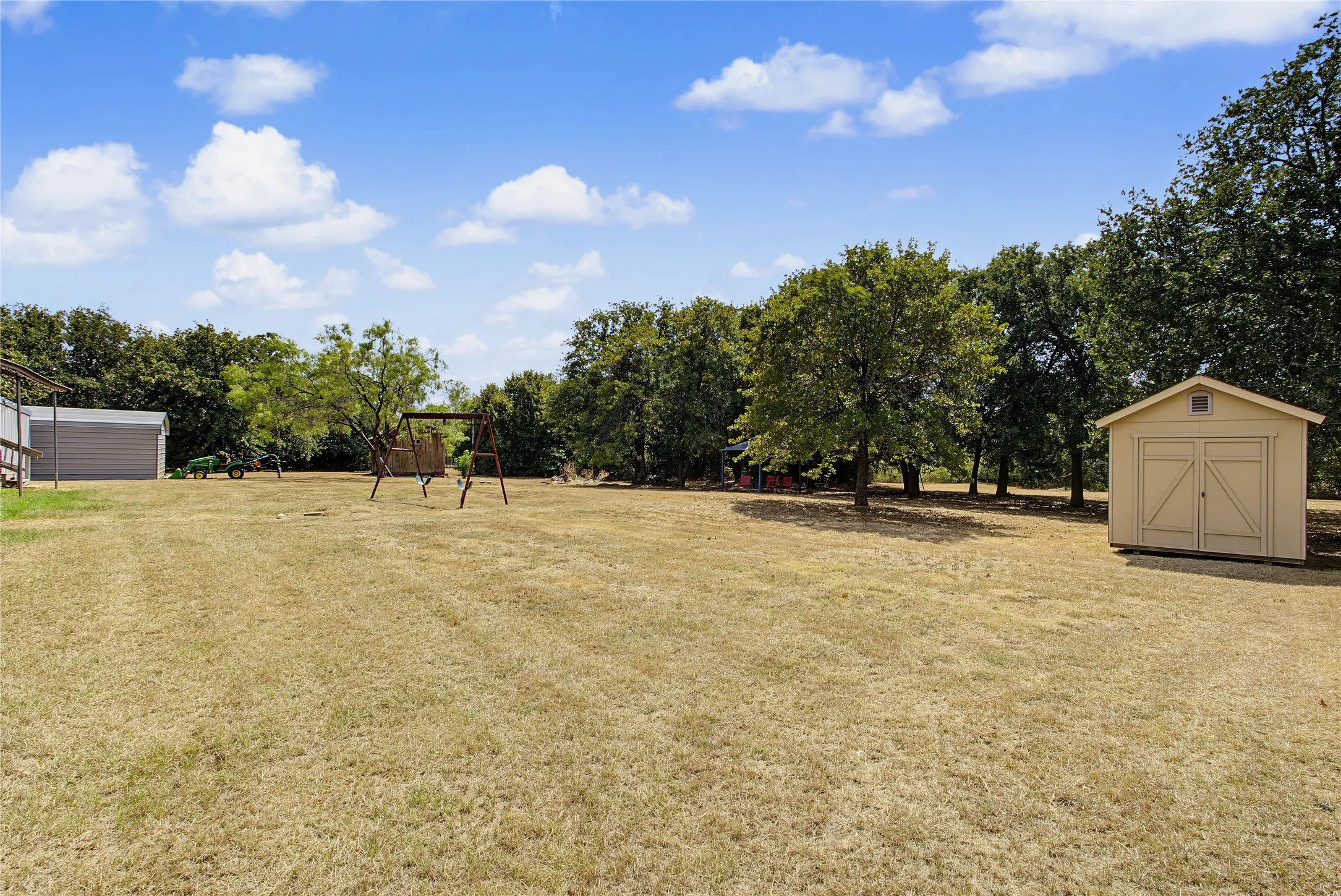Expansive outdoor area featuring a large lawn, mature trees, and a detached storage shed