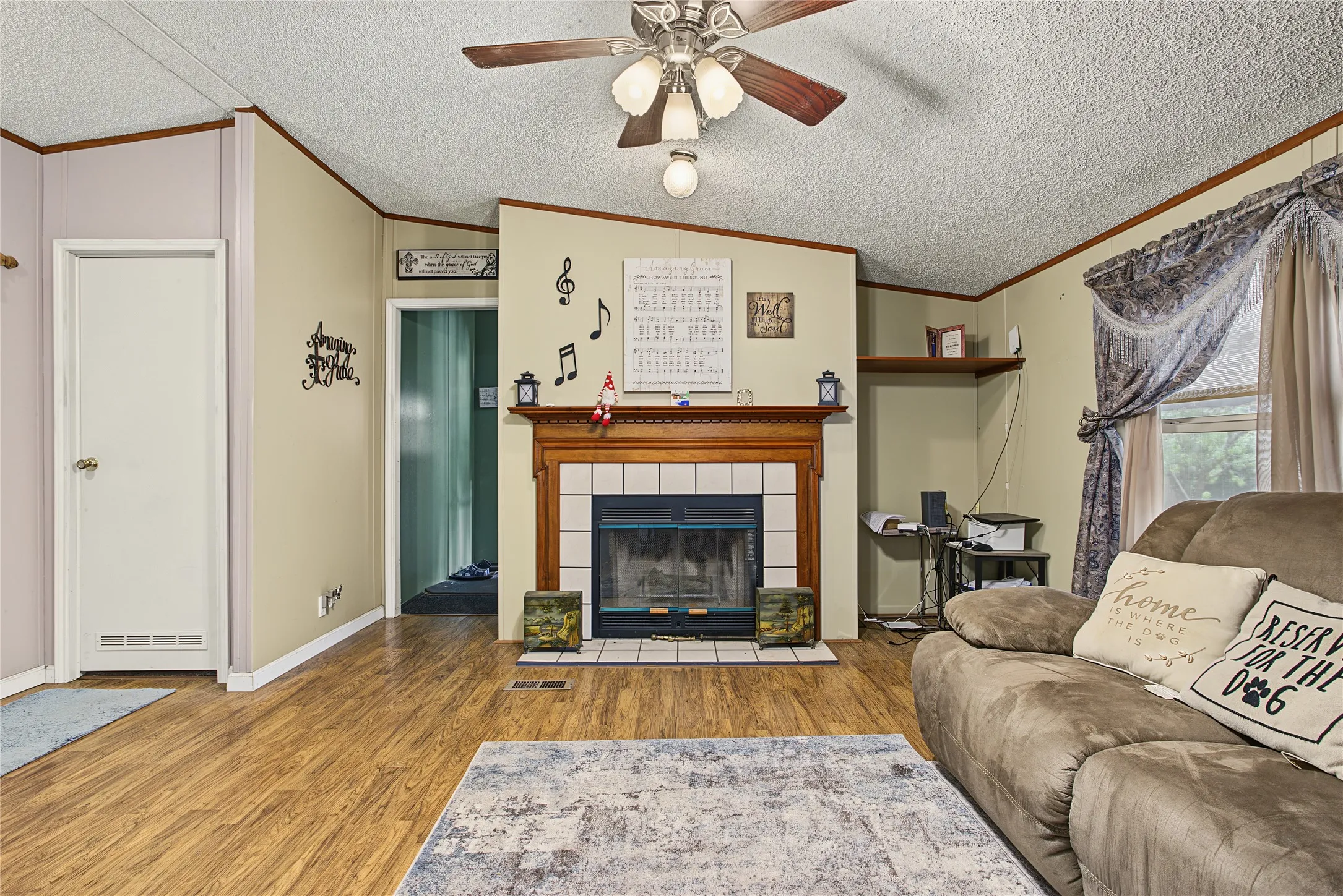 Wood-finish flooring, ceiling fan with light fixture, and a fireplace with a wood mantel and tile surround