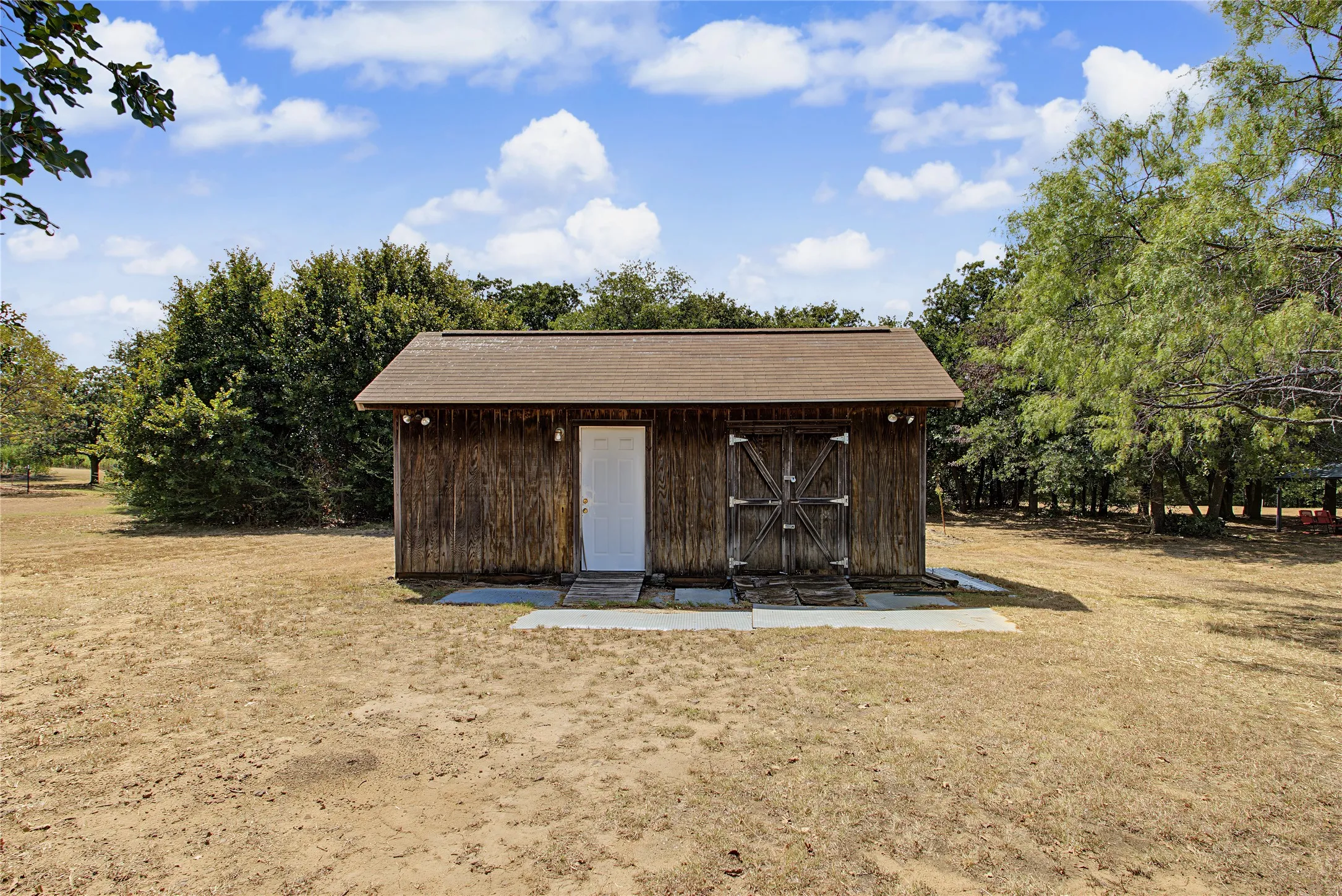 Wood-sided outbuilding with a gabled roof, a white entry door, and double barn doors