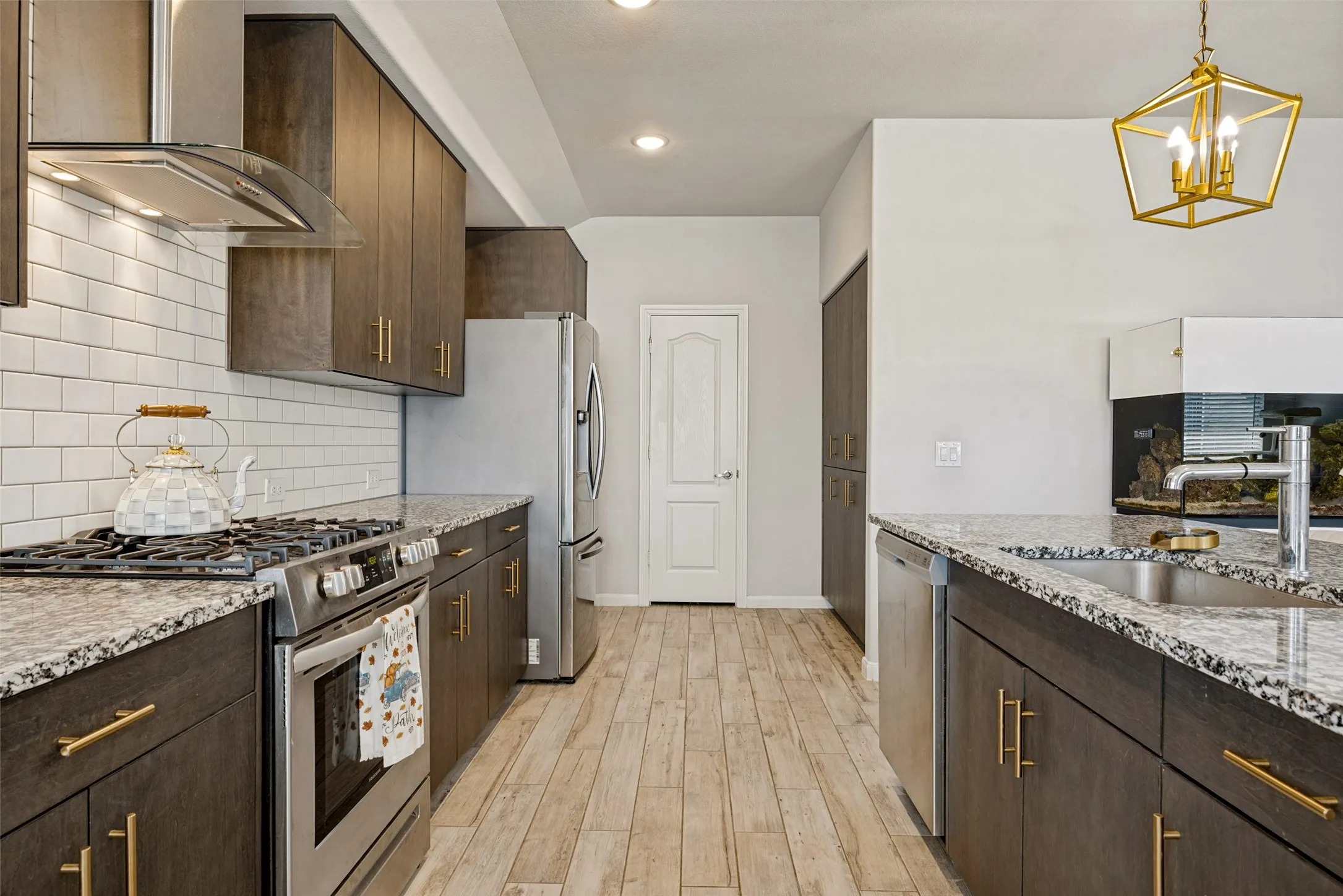 Contemporary kitchen featuring dark wood-finish cabinetry, light-toned countertops, stainless steel appliances, and a subway tile backsplash