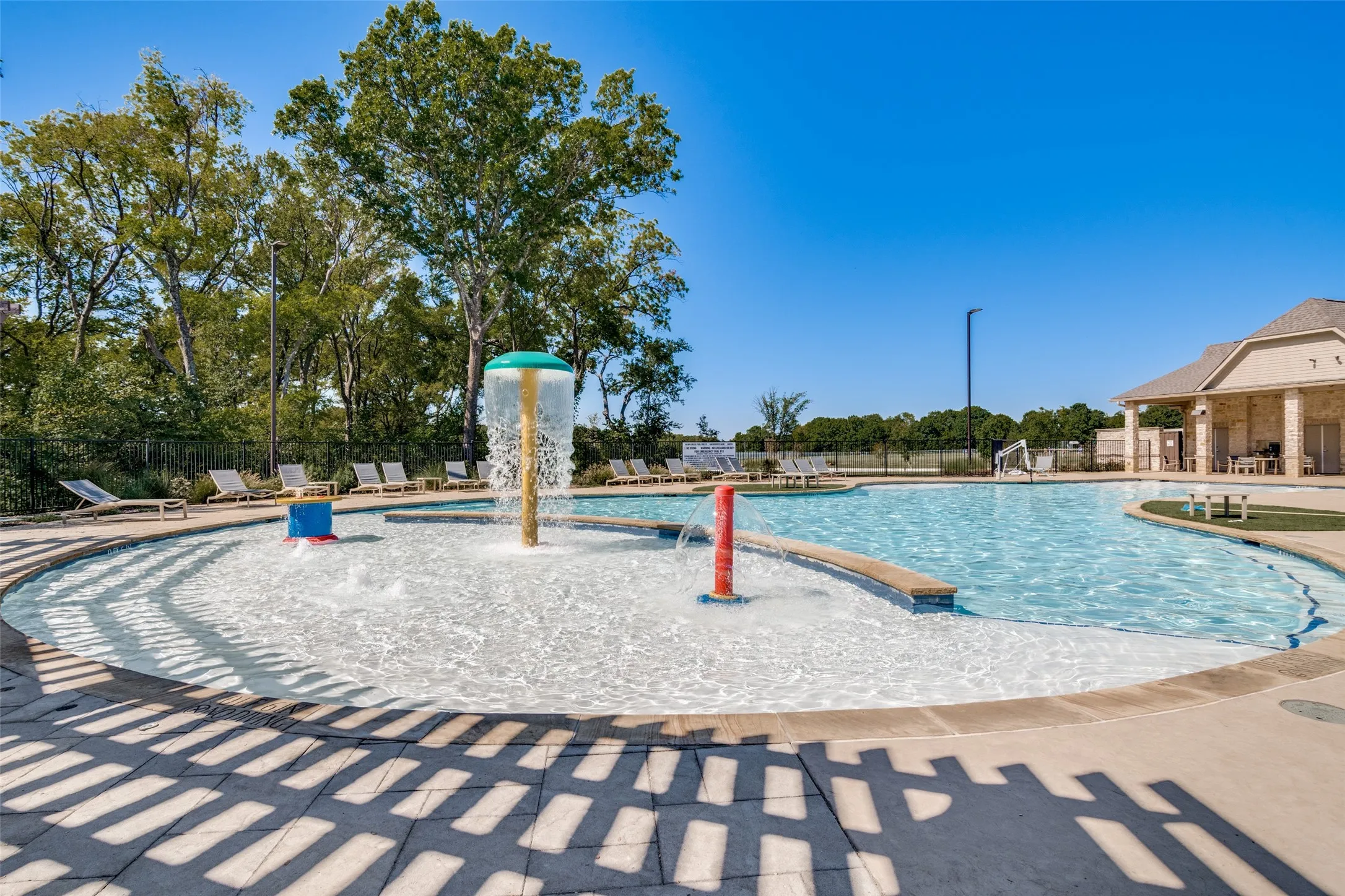 Resort-style pool area featuring a curved swimming pool, dedicated splash pad with water features, and a covered lounge area