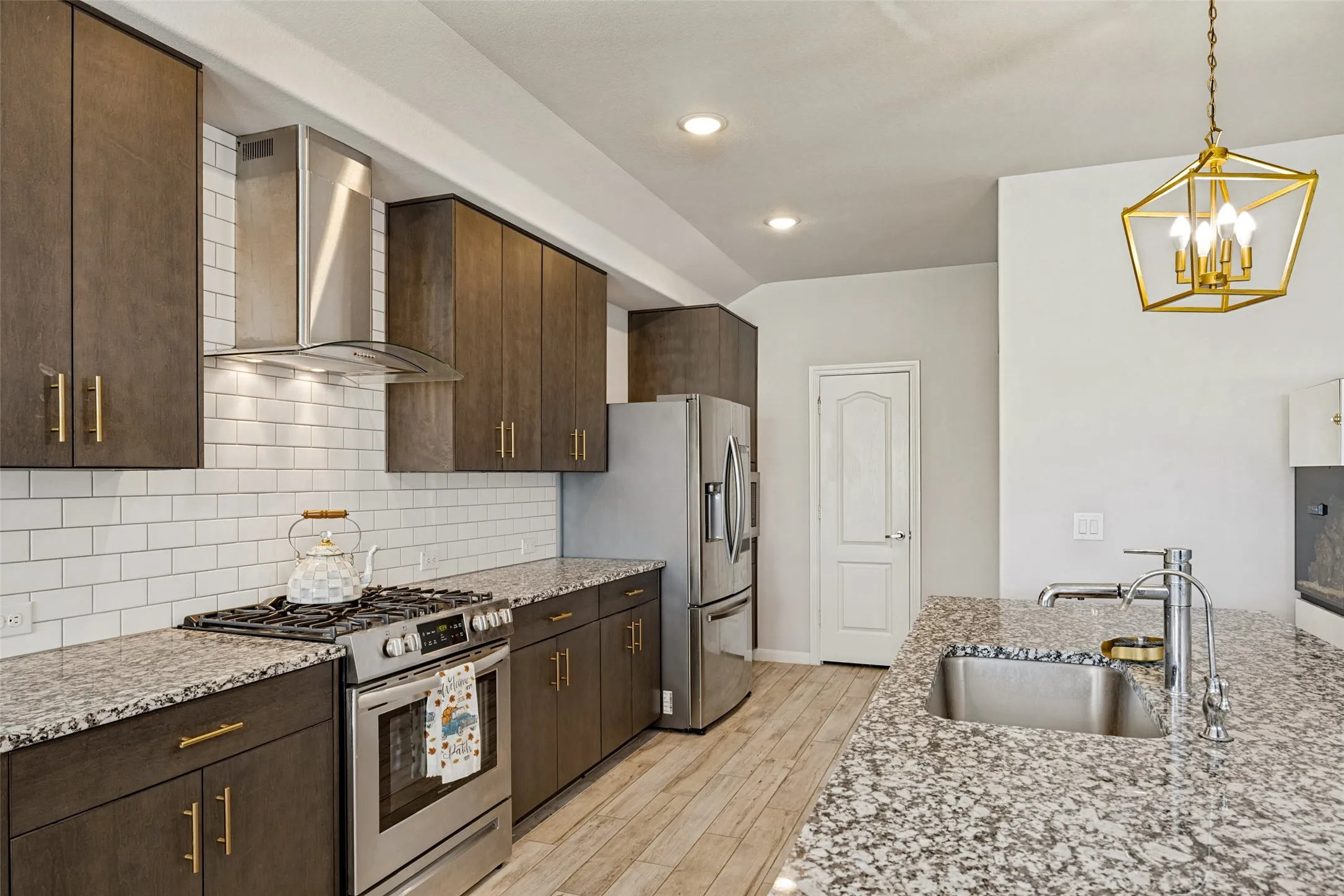 Kitchen featuring wood-finish cabinetry, stainless steel appliances, granite countertops, white subway tile backsplash, and recessed lighting