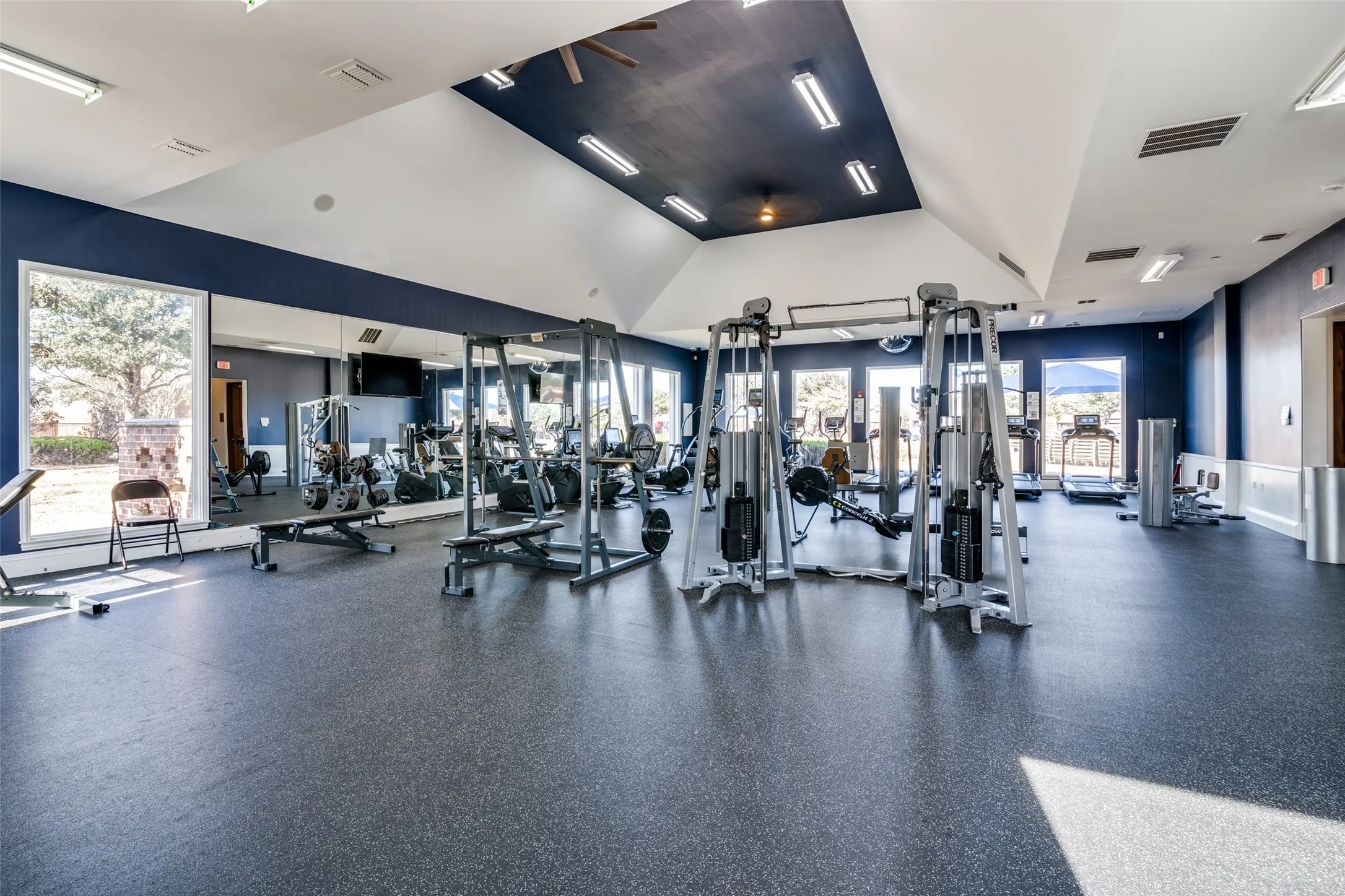 Spacious fitness center featuring high ceilings, rubberized flooring, mirrored walls, and large windows