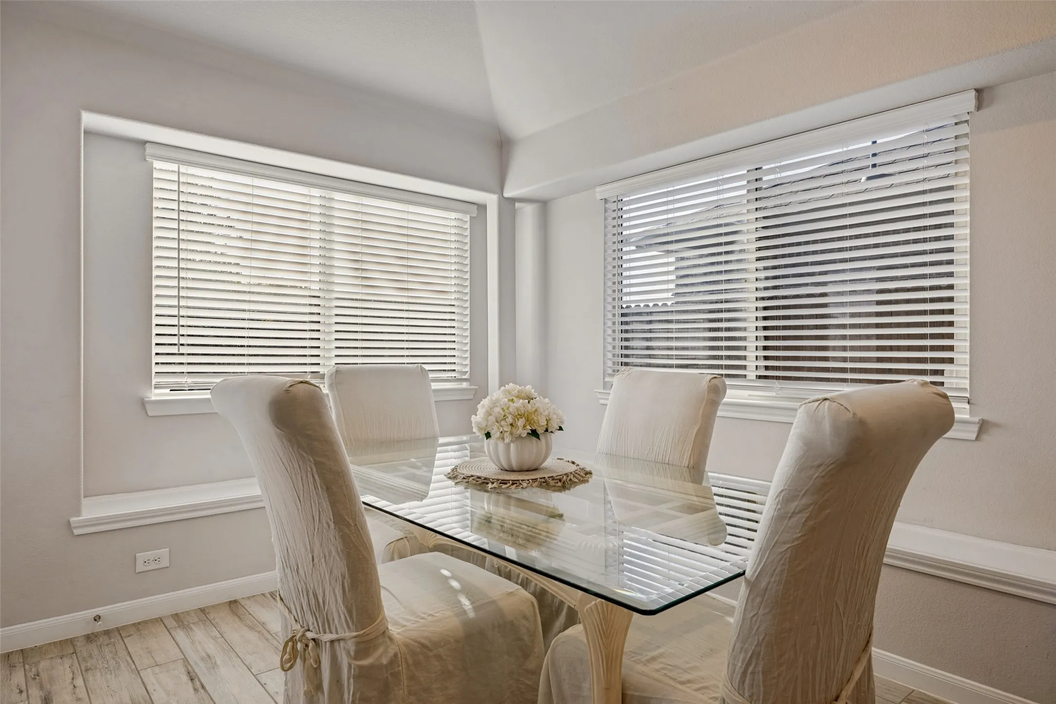 Windowed dining area featuring wood-finish flooring, corner windows, and horizontal blinds