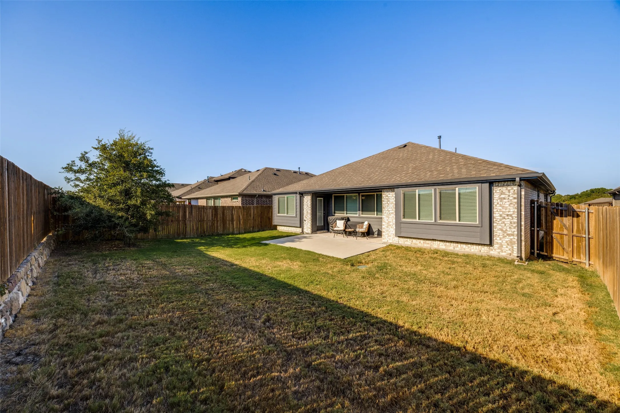 Expansive fenced backyard with a concrete patio, brick exterior, and a wood privacy fence