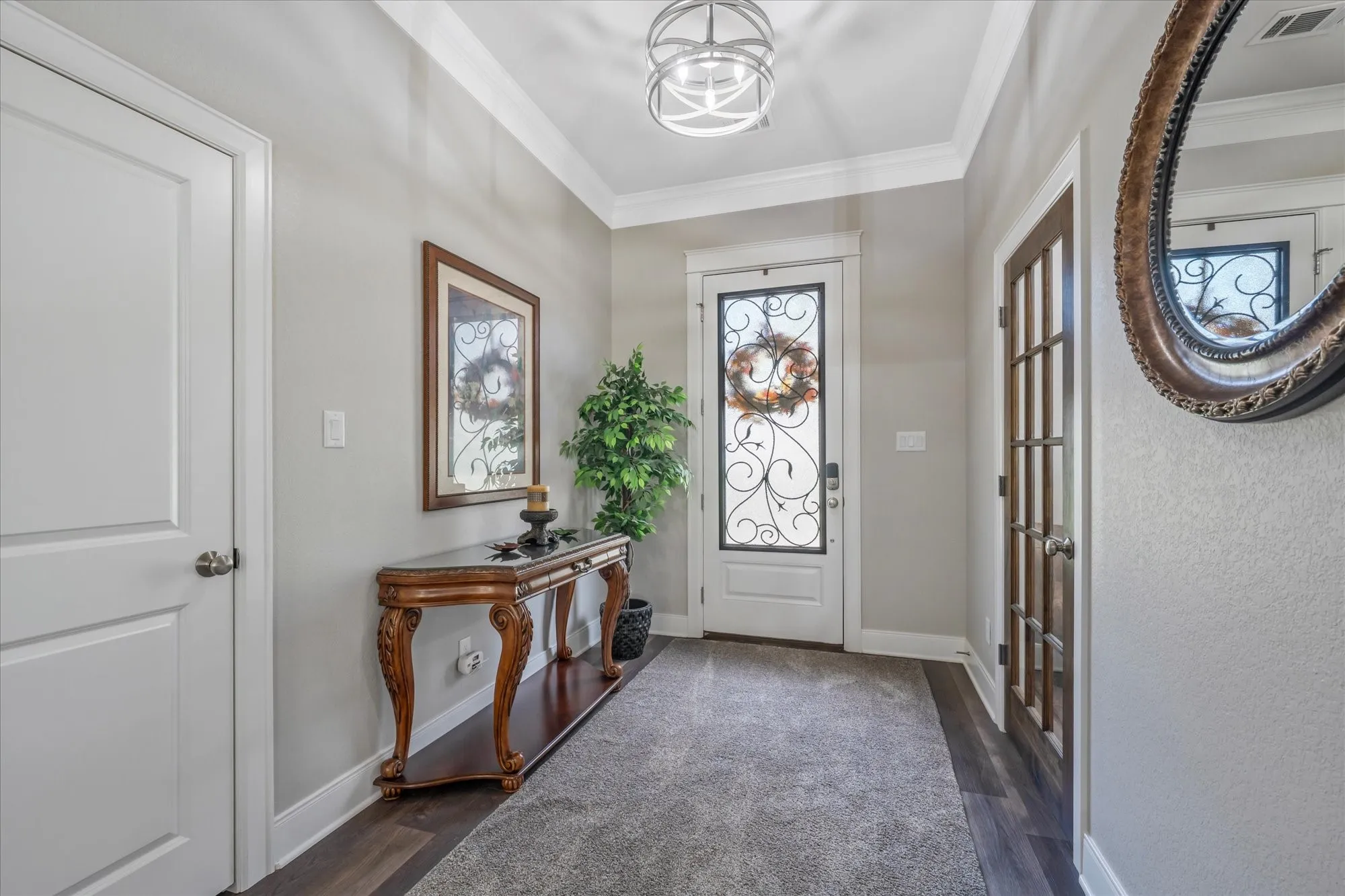 Decorative front door with wrought iron detailing, crown molding, a modern semi-flush mount light fixture, wood-finish flooring, and a paneled interior door