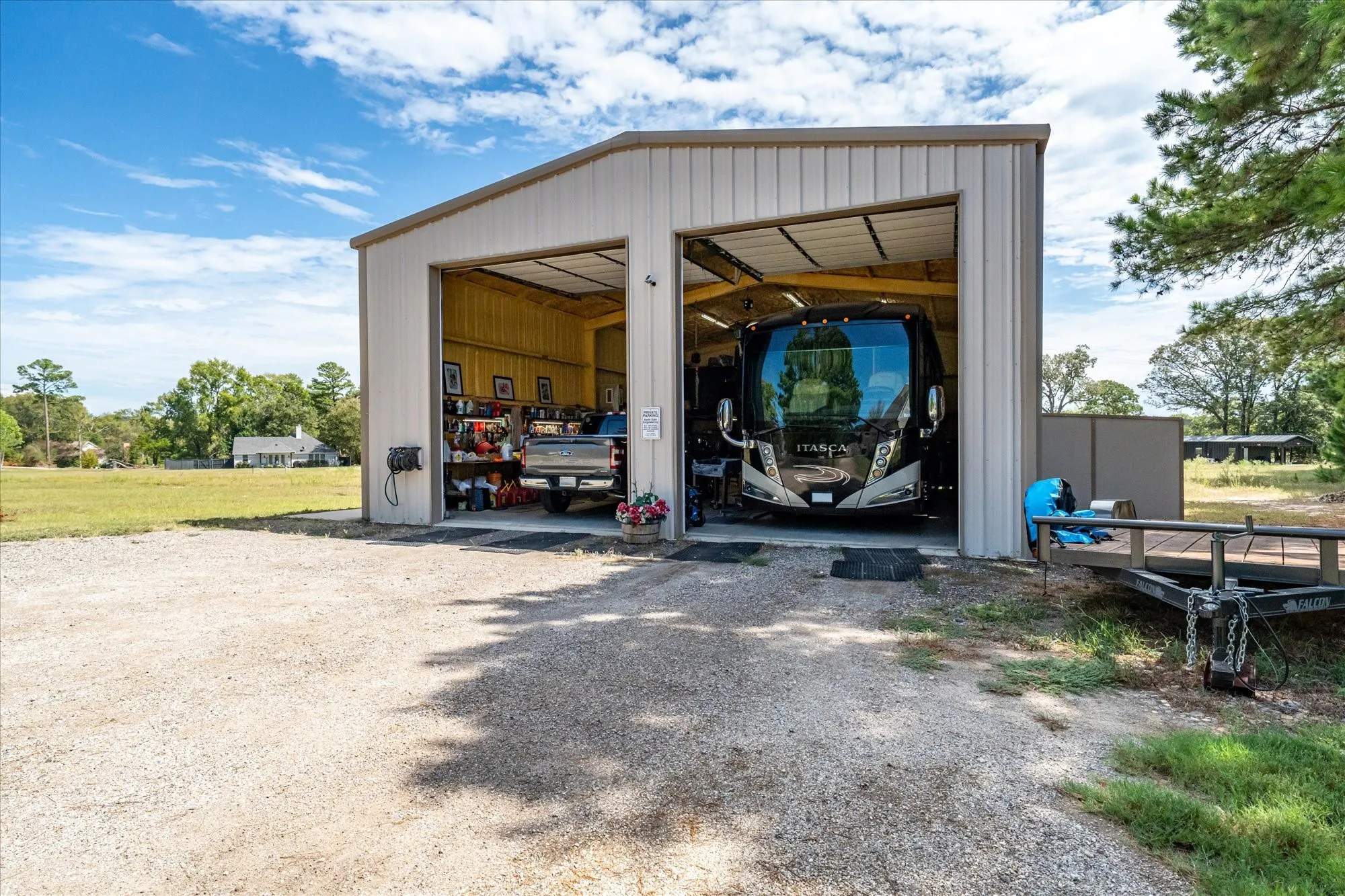 Two-bay metal structure with roll-up doors, gravel driveway, and a partially visible utility shed