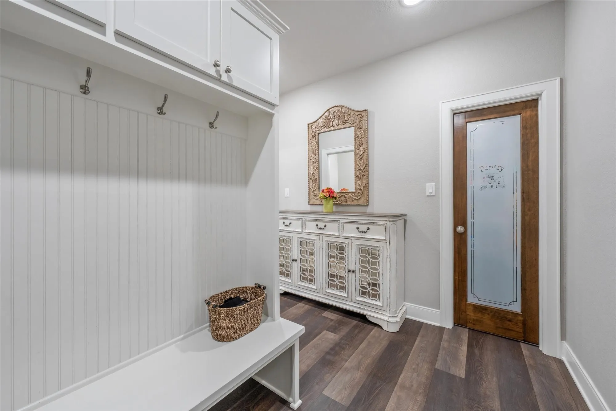 Built-in storage bench with beadboard paneling, upper cabinetry, and integrated coat hooks
