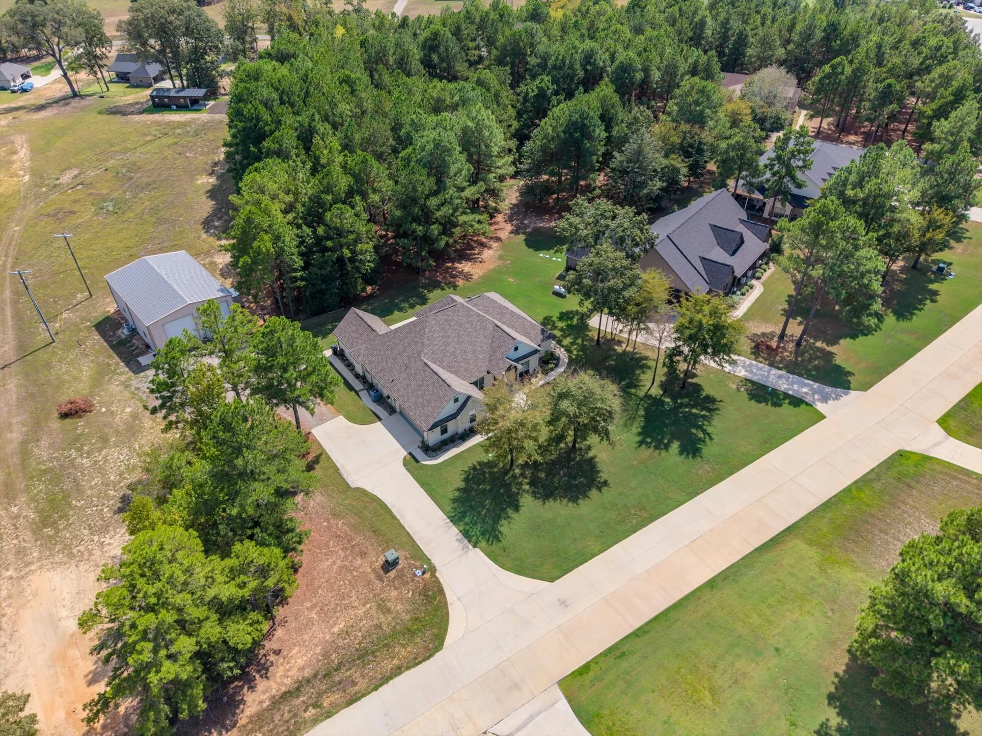 Expansive property featuring a single-story residence, separate metal-roofed outbuilding, concrete driveway, and mature trees