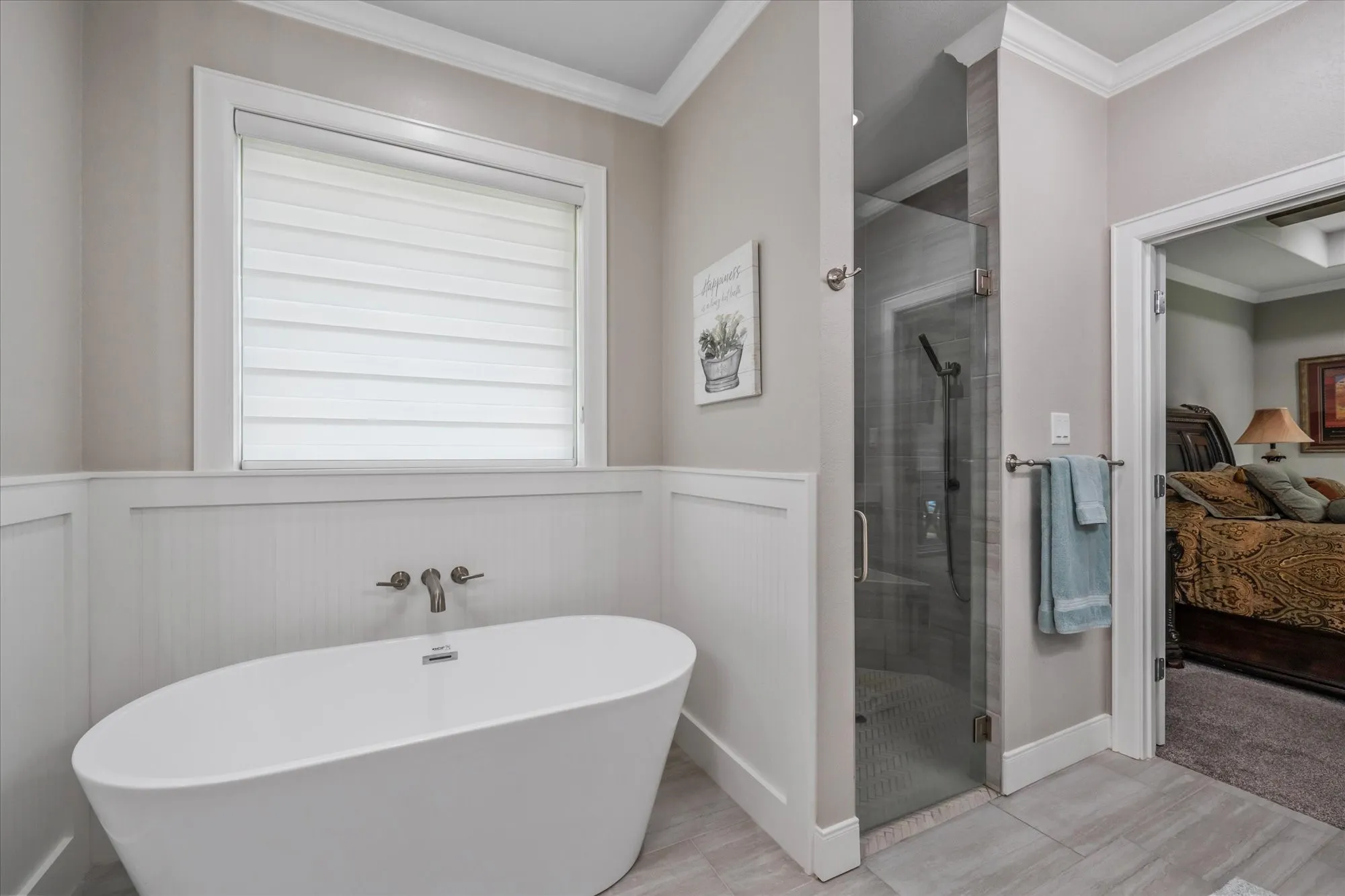 Freestanding soaking tub with a wall-mounted faucet, glass-enclosed shower, and wainscoting paneling