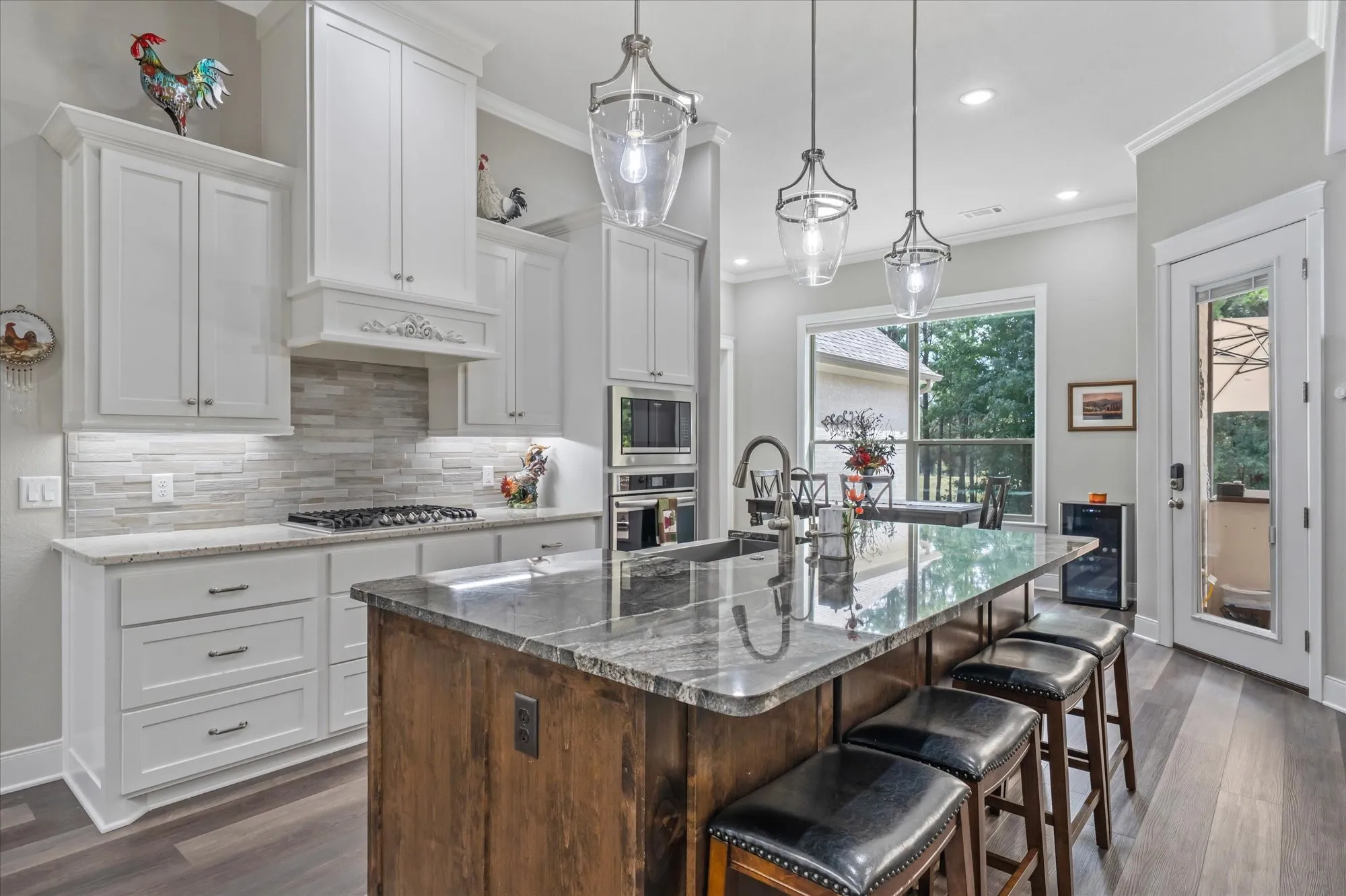 Kitchen featuring white shaker-style cabinetry, granite countertops, a gas range, stainless steel built-in appliances, and a central island with seating