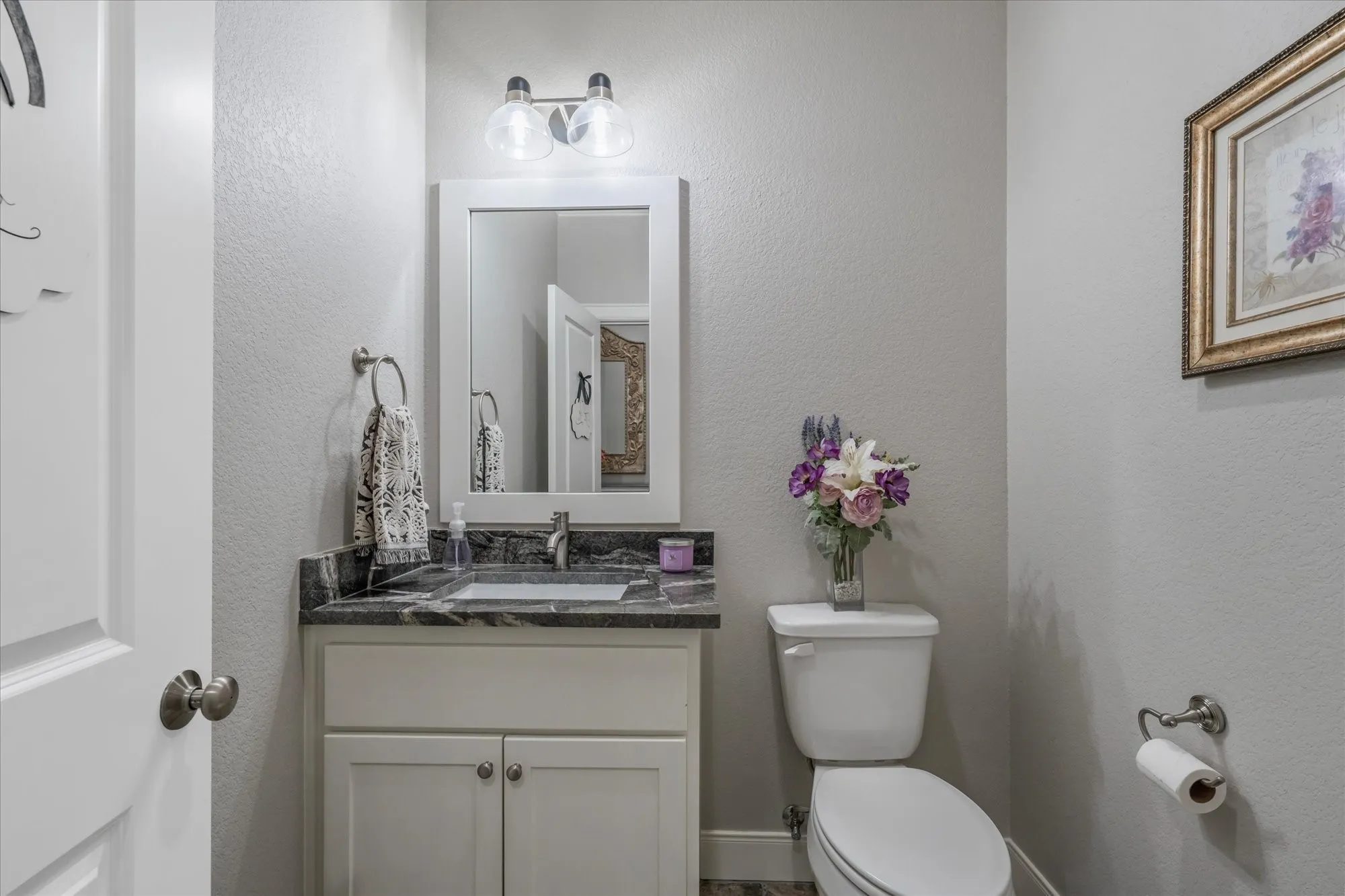 White vanity with undermount sink, dark stone countertop, and two-light vanity fixture