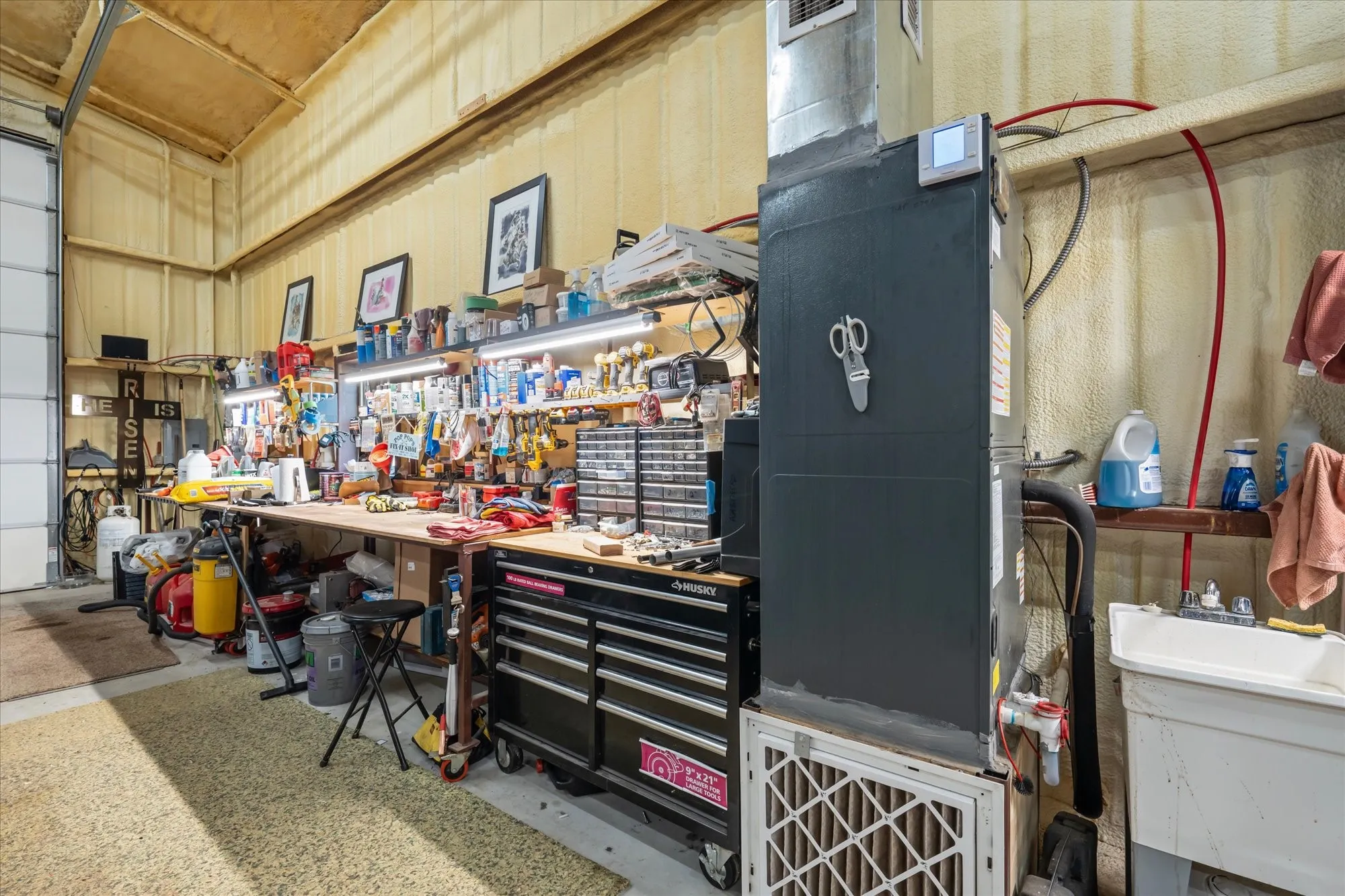 Utility sink with a wall-mounted faucet, dedicated workbench with overhead lighting, and exposed ductwork