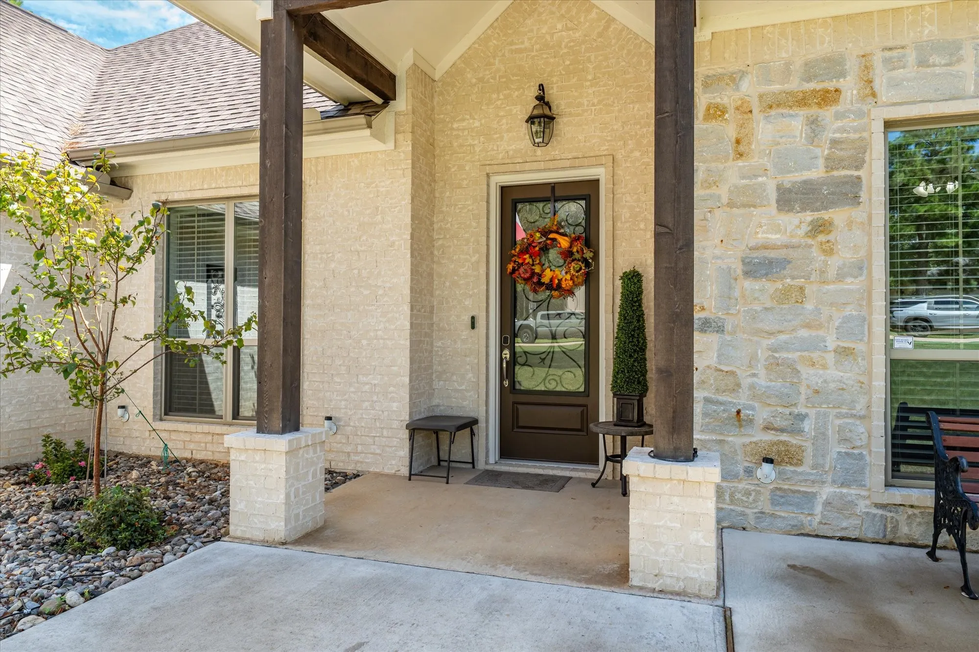 Covered front entry featuring stone and stucco exterior, wood support columns, and a solid wood entry door with decorative glass
