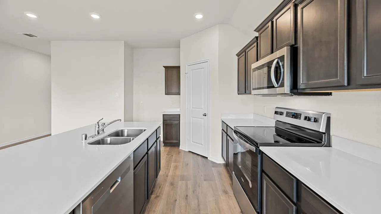 Kitchen featuring an island with a double basin sink, dark wood-finish cabinetry, light-toned countertops, stainless steel appliances, and wood-finish flooring