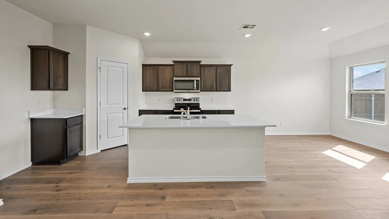 Open-concept living area with wood-finish flooring, recessed lighting, and a kitchen island featuring a sink
