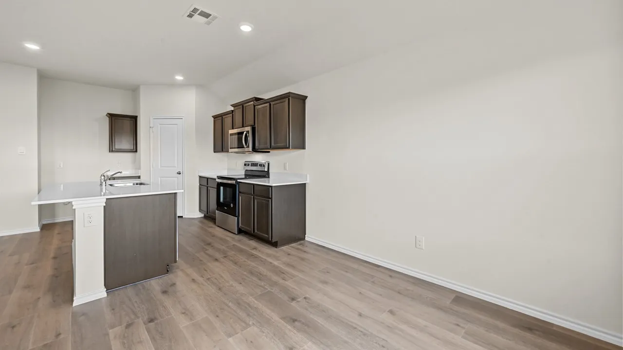 Kitchen featuring dark wood-finish cabinetry, stainless steel appliances, a kitchen island with a single-basin sink, and recessed lighting