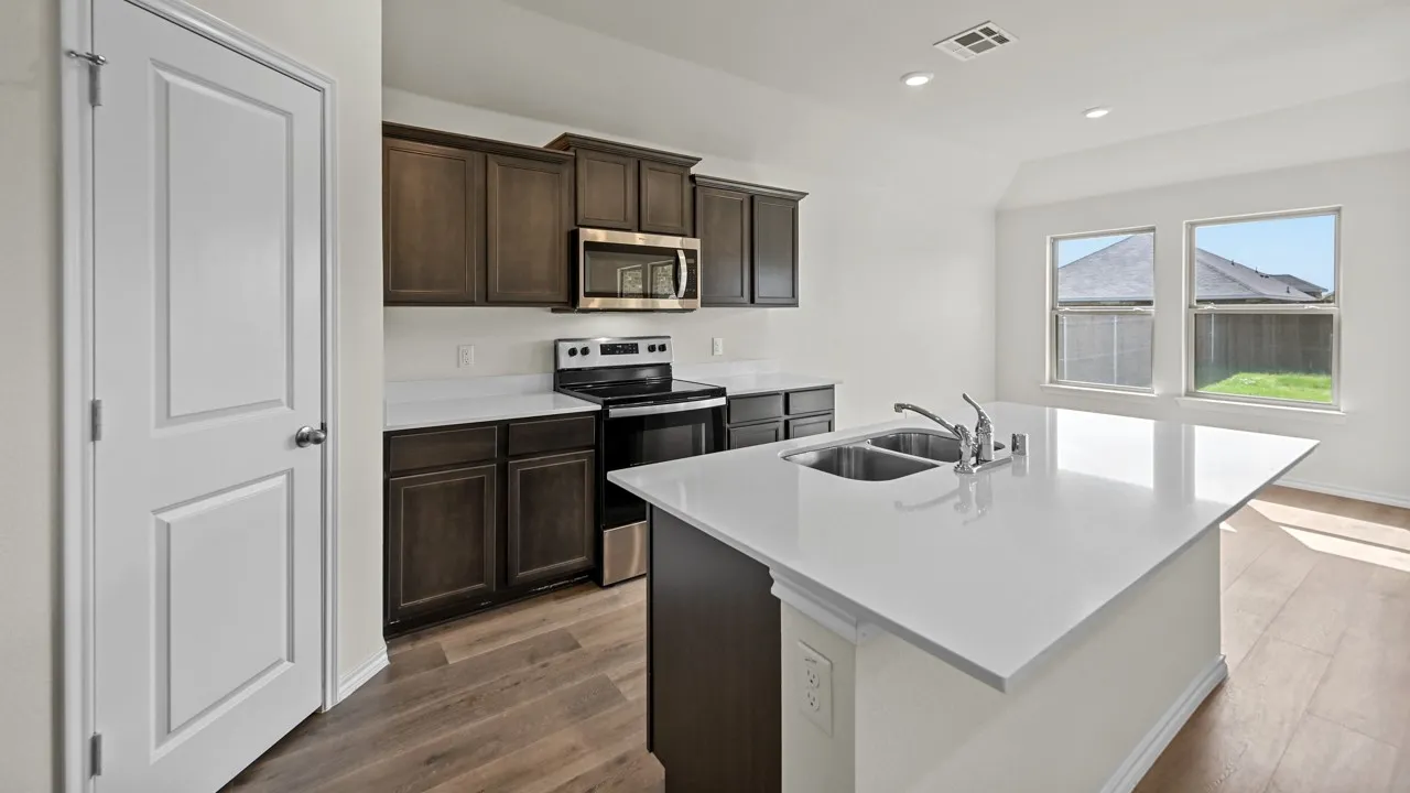 Kitchen featuring dark wood-finish cabinetry, stainless steel appliances, a center island with double basin sink, white countertops, and wood-finish flooring