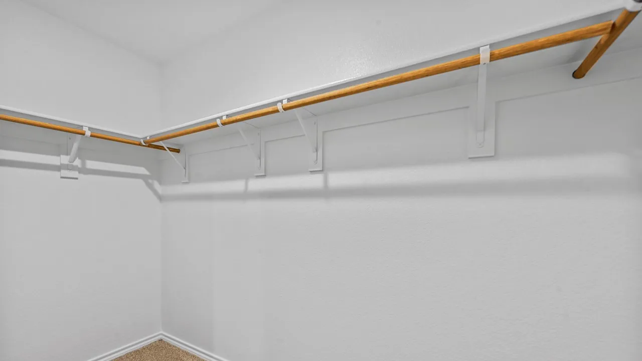 Walk-in closet featuring wood-finish hanging rods, white wall-mounted supports, and light-toned carpet flooring