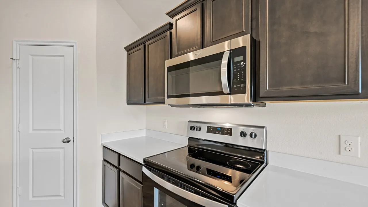 Stainless steel microwave and range, dark wood-finish cabinetry, and white countertops