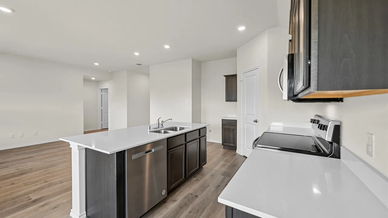 Spacious kitchen featuring an island with dual sinks, stainless steel appliances, white countertops, and dark wood-finish cabinetry
