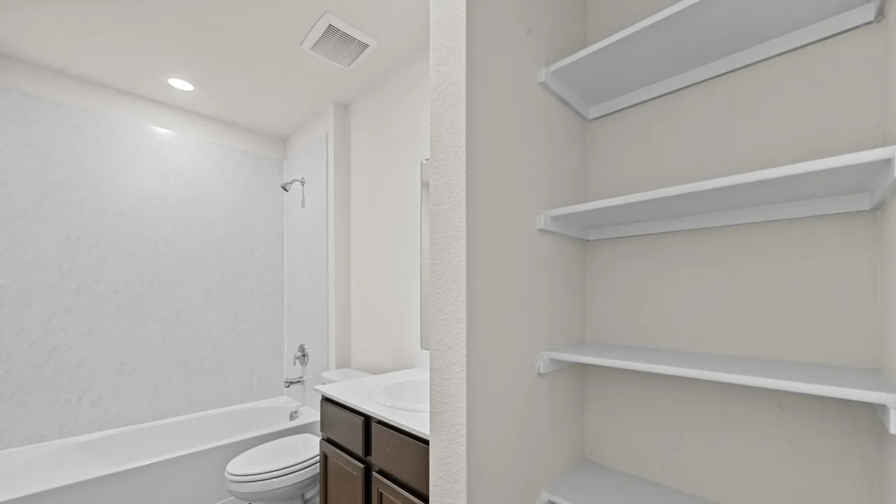 Tub and shower combination with chrome fixtures, single vanity with a white countertop, and built-in shelving