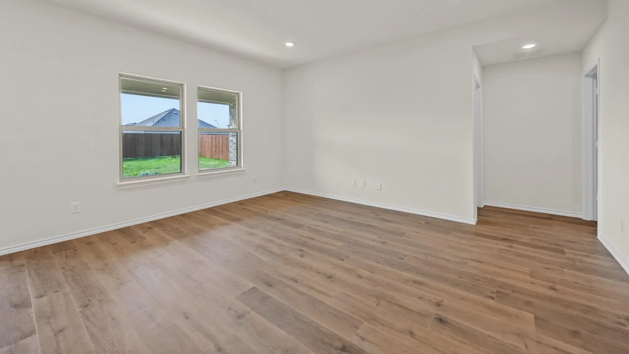 Spacious interior room with wood-finish flooring, two large windows, white walls, and recessed lighting