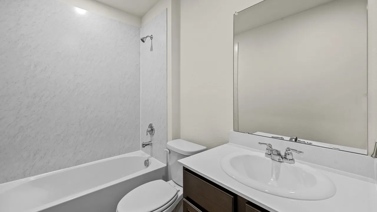Bathroom featuring a white bathtub, shower with a textured surround, single vanity with an integrated sink, and a framed mirror