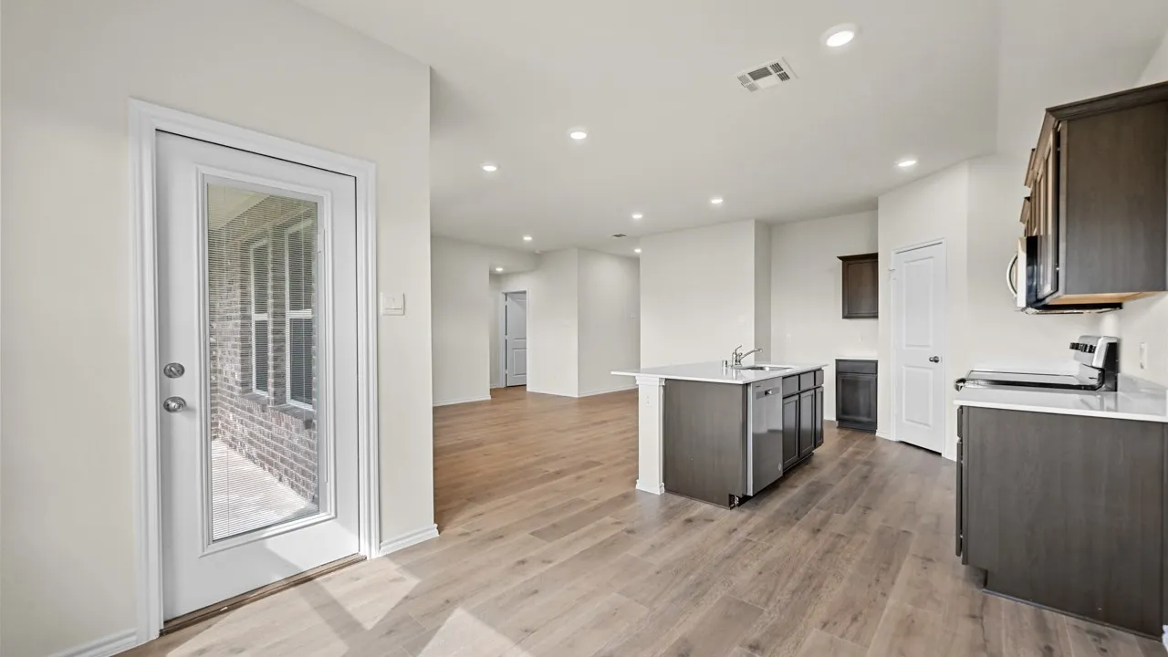Kitchen featuring dark wood-finish cabinetry, light-toned countertops, a central island with an integrated sink, stainless steel appliances, and wood-finish flooring
