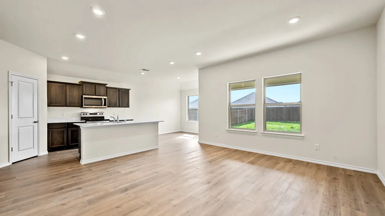 Open-concept living space featuring wood-finish flooring, recessed lighting, a kitchen island with a basin sink, dark wood-finish cabinetry, and stainless steel appliances
