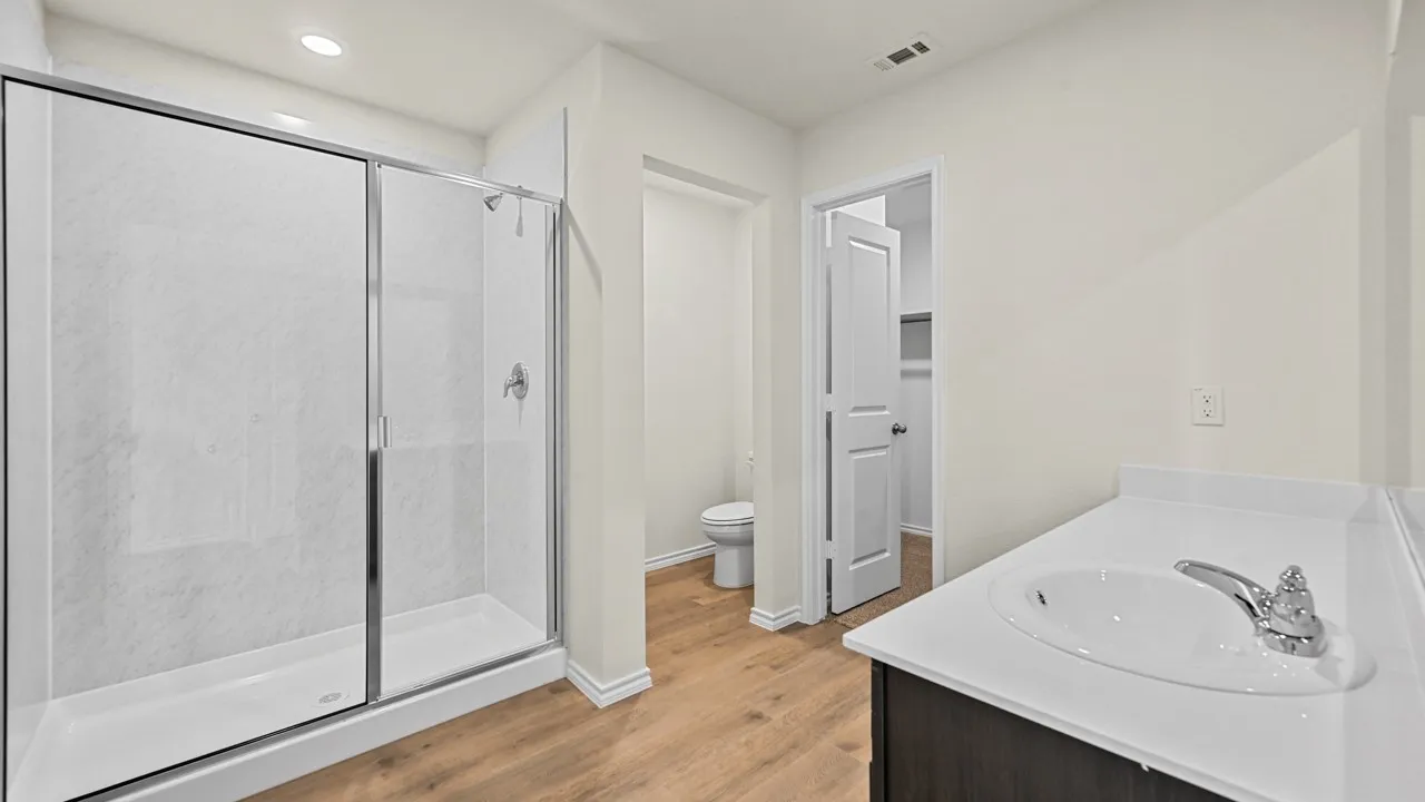 Glass-enclosed shower with white surround, single vanity with integrated sink, chrome faucet, and wood-finish flooring