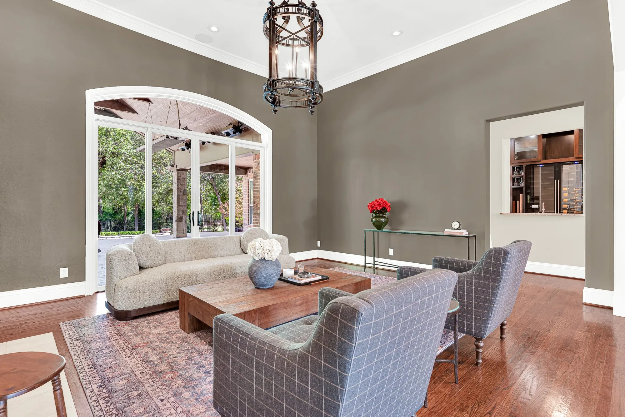 A wide arched glass doorway frames leafy outdoor views, pouring natural light against rich taupe walls. Imagine curling up with a book as soft afternoon light warms the room.