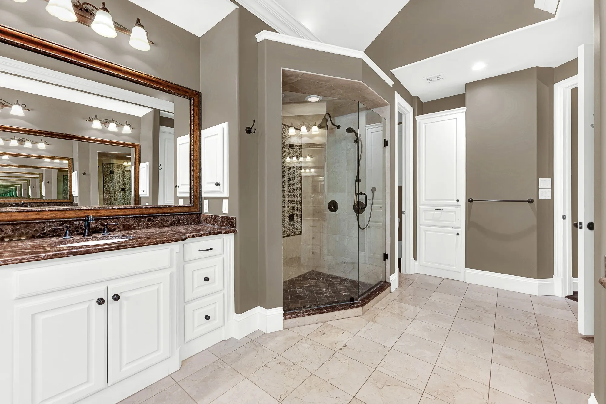 An angled, frameless glass walk-in shower showcases custom tilework that reflects brightness across vanity mirrors. Start your day energized under a warm stream of water in this airy space