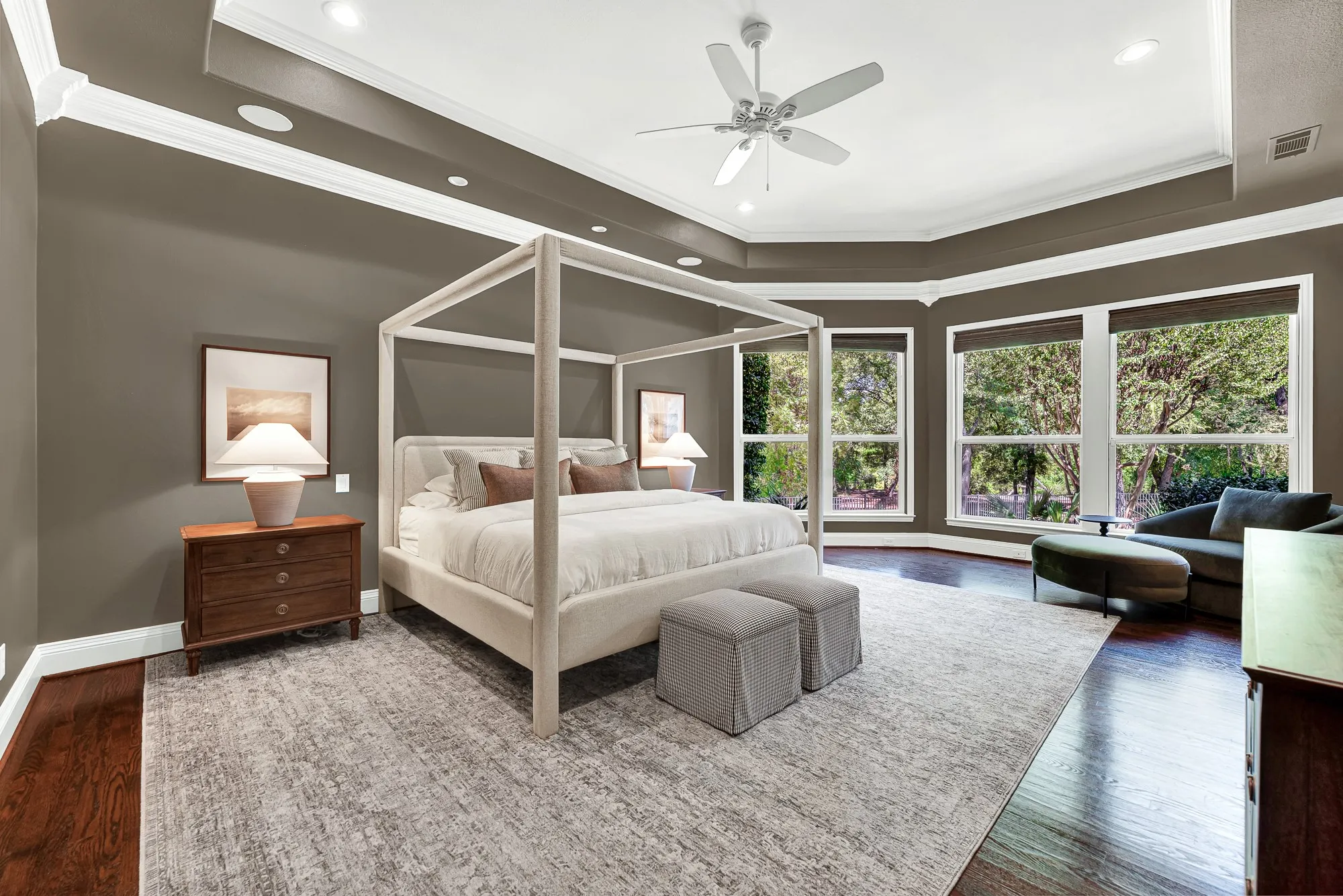 Deep tray ceiling molding and wide picture windows surround the suite with peaceful garden views. Wake up slowly to soft morning light filtering through private, tree-lined glass panes.