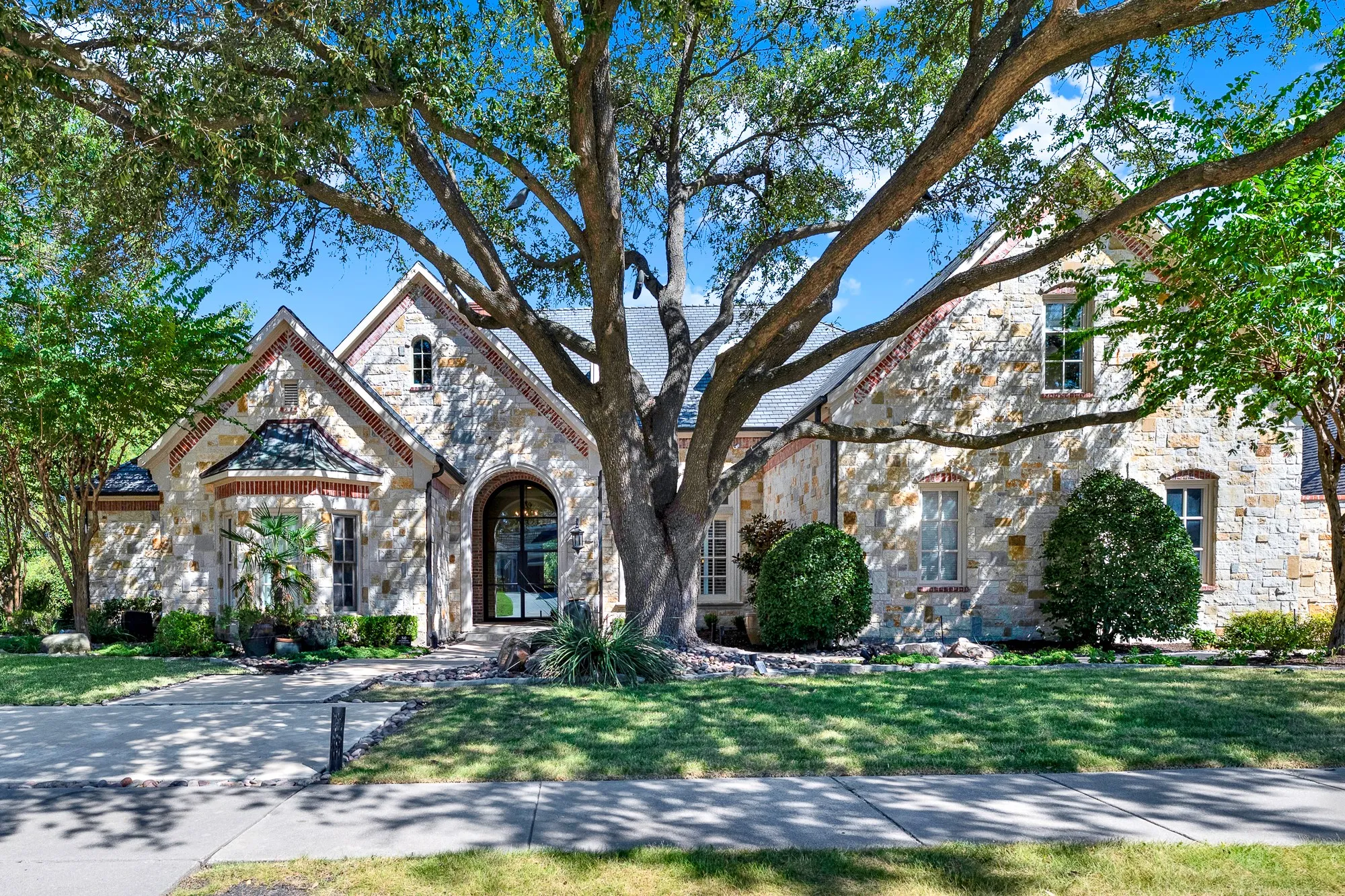  A magnificent mature oak arches over the rustic stone facade, filtering dappled sunlight across the grand entry. Arriving home feels like entering a private, tranquil estate every single afternoon.