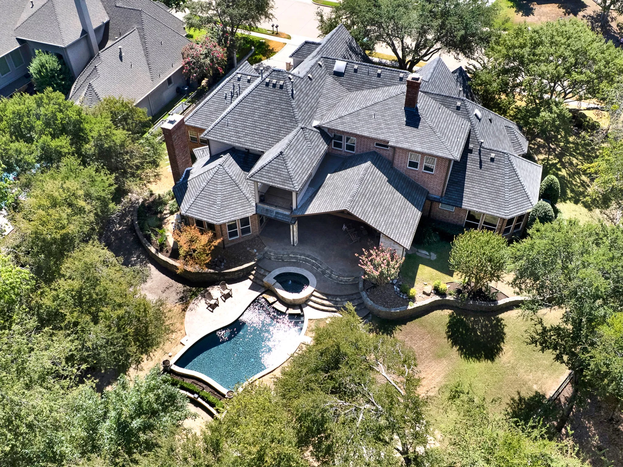 Welcome to 5237 Sky Lake. Prominent brick chimneys accent multi-angled rooflines that frame an inviting poolside patio space. Enjoy quiet evening cocktails while watching afternoon sun shadows stretch across stone terraces