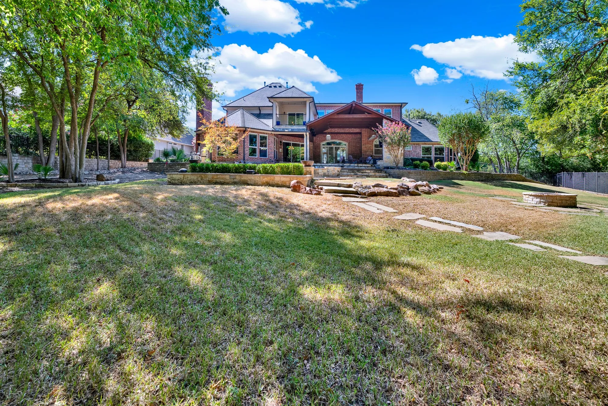 Tiered stone retaining walls step up toward the multi-level brick residence framed by expansive lawn. Imagine kids playing outdoor games across the grass before gathering for dinner on the porch.