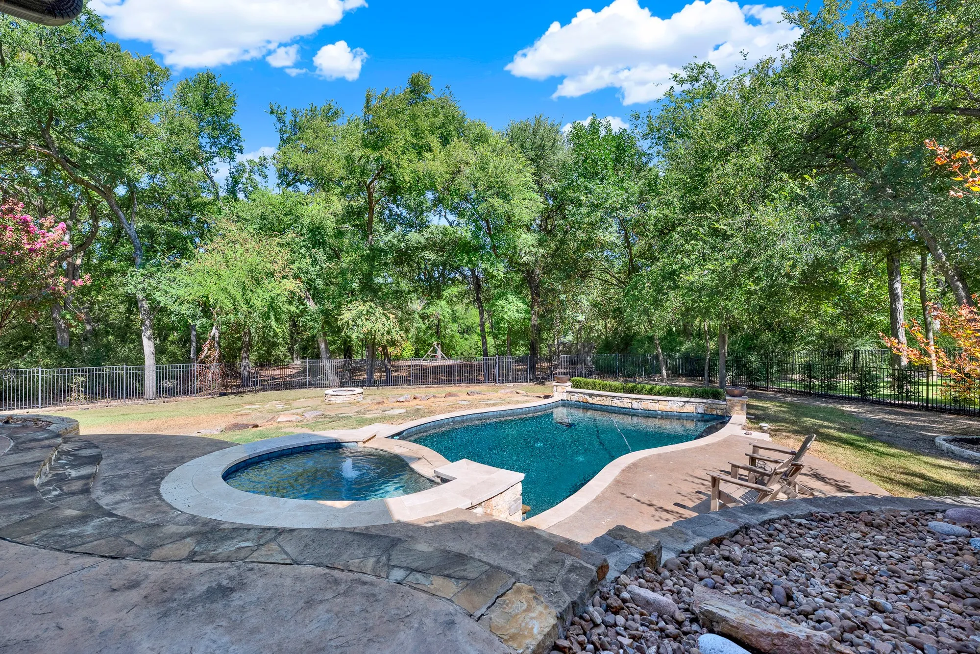 Curving stone coping defines a sparkling pool and spa set against a lush, forest-like tree line. Spend sunny summer afternoons floating lazily while listening to breeze rustling through the canopy.